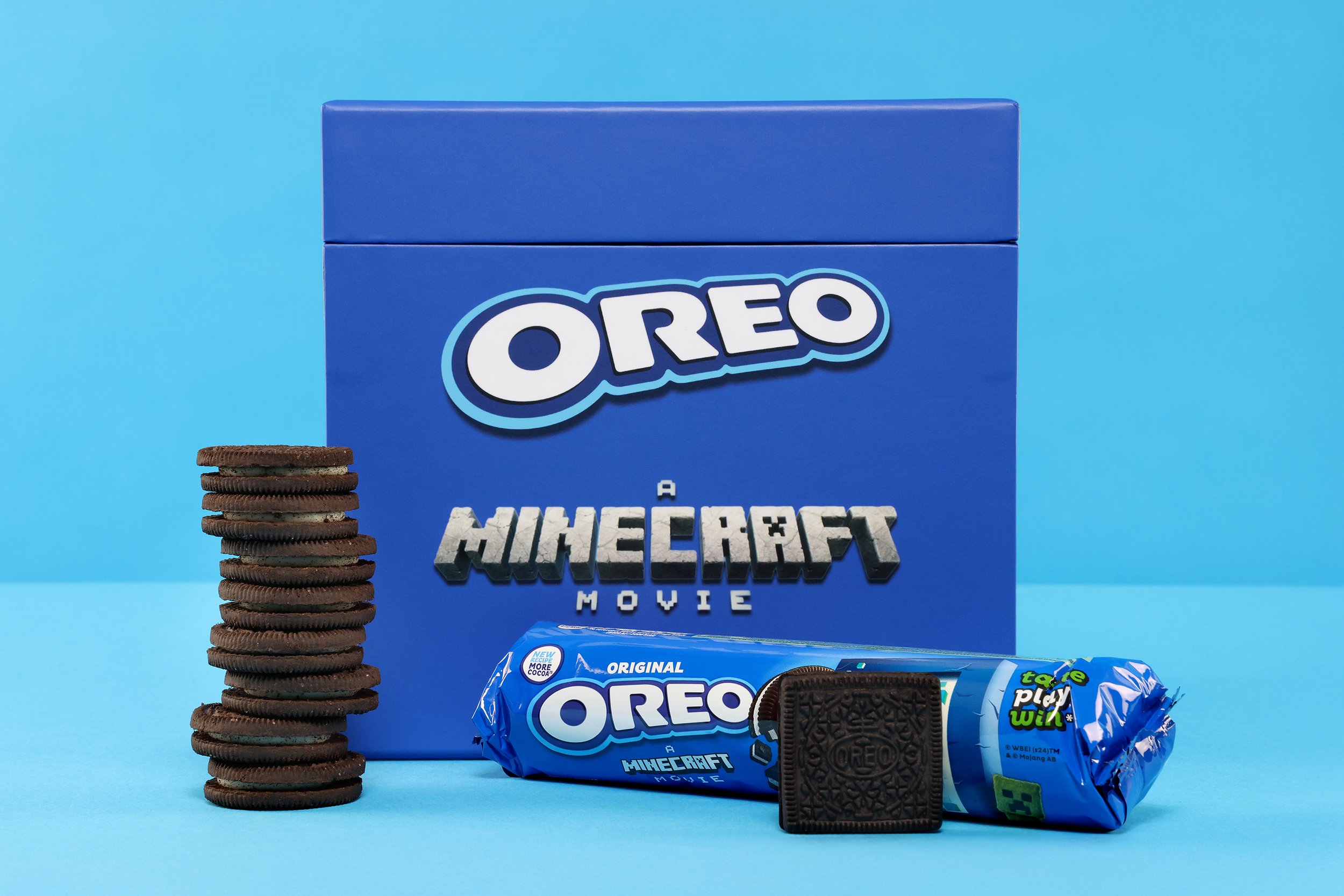 A blue Oreo cookie box with a Minecraft movie logo, a stack of Oreo cookies, and a pack of Oreo cookies with a single cookie in front, all set against a light blue background.