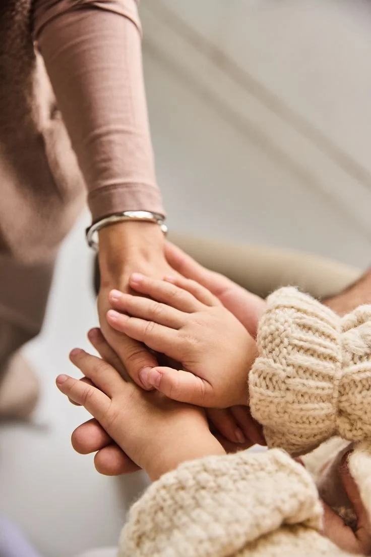 Een volwassene houdt twee jonge kinderen bij de hand, mogelijk tijdens een activiteit of knuffel.