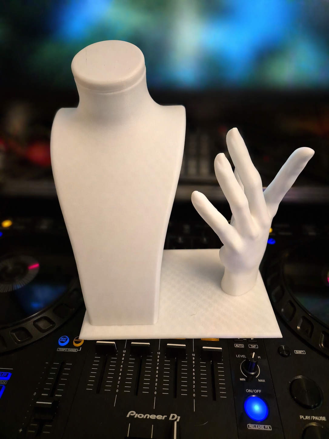A white mannequin bust and a white hand sculpture on a white display stand, placed on a DJ mixer.