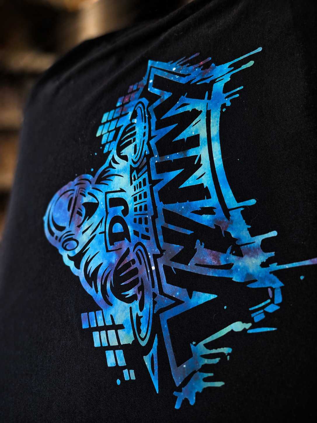 Close-up of a black T-shirt with a neon-style graphic design featuring a lion wearing sunglasses, the words 'DAD' and 'STANCE' in stylized font, set against a dark background.