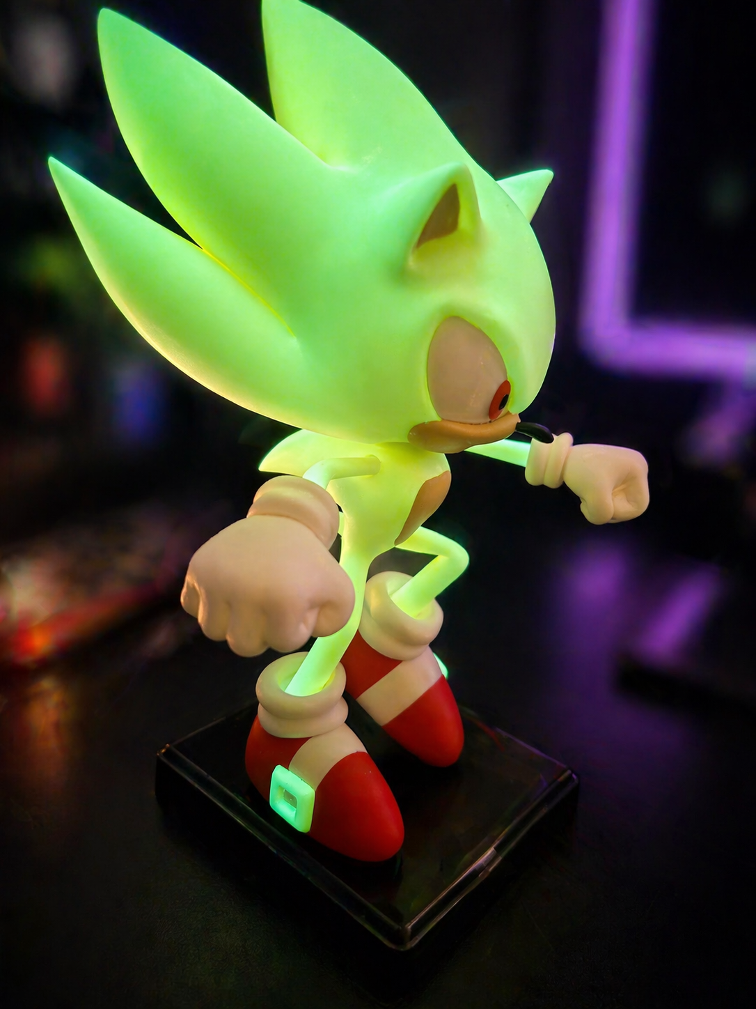 A glowing green Sonic the Hedgehog figure with closed eyes, sticking out tongue, red shoes, standing with an arm on hips and the other bent, with a dark background.