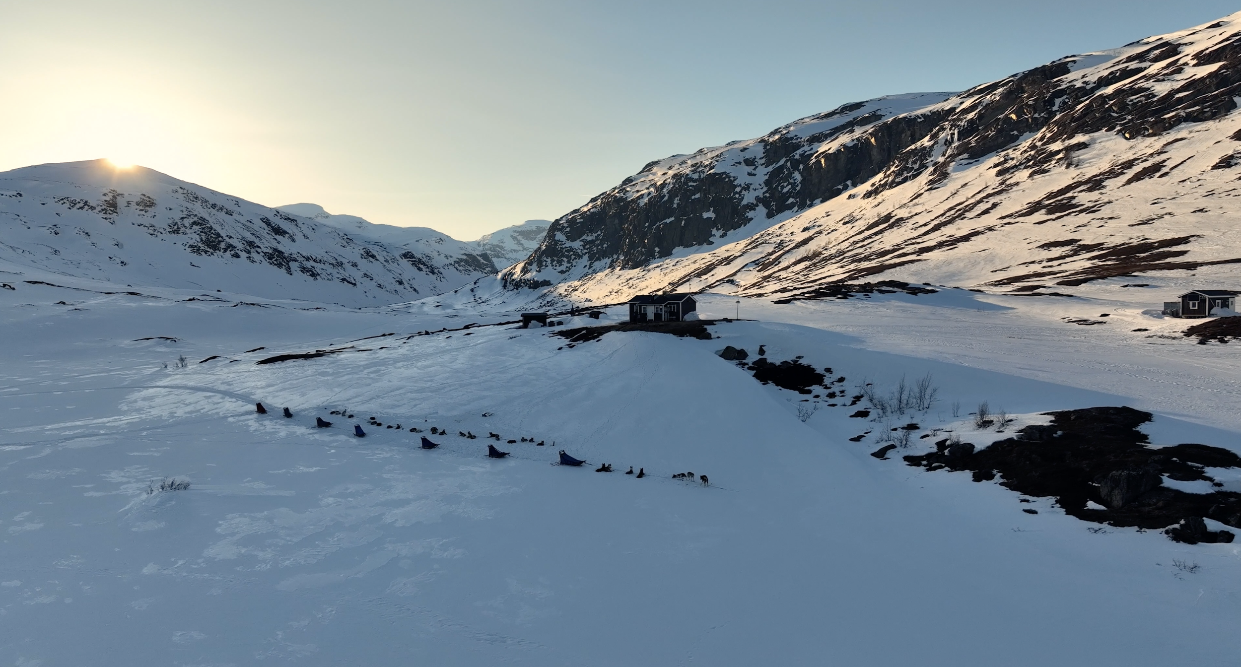 Schneebedechte Berge mit Sonnenaufgang, Häuser und Hundespur im Schnee