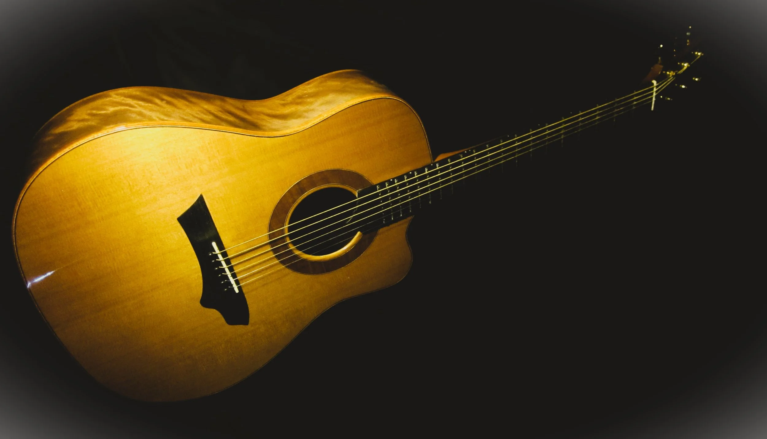 An acoustic guitar with a natural wood finish, resting against a dark background.