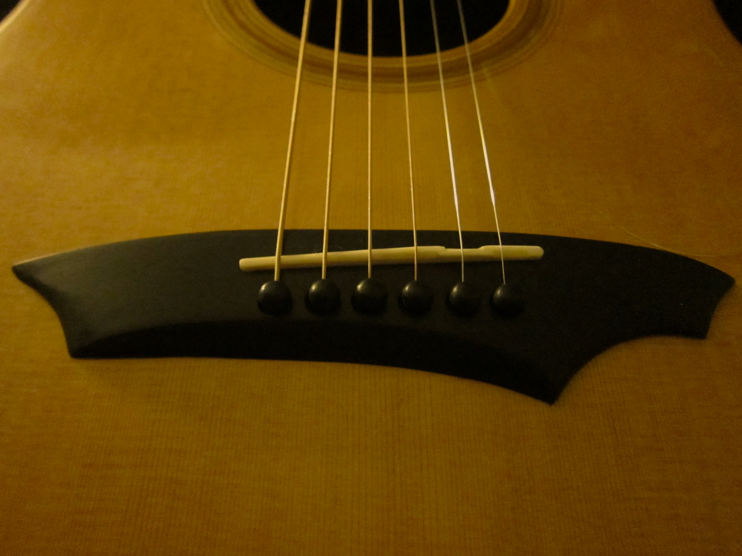 Close-up of the bridge, strings, and sound hole of an acoustic guitar.
