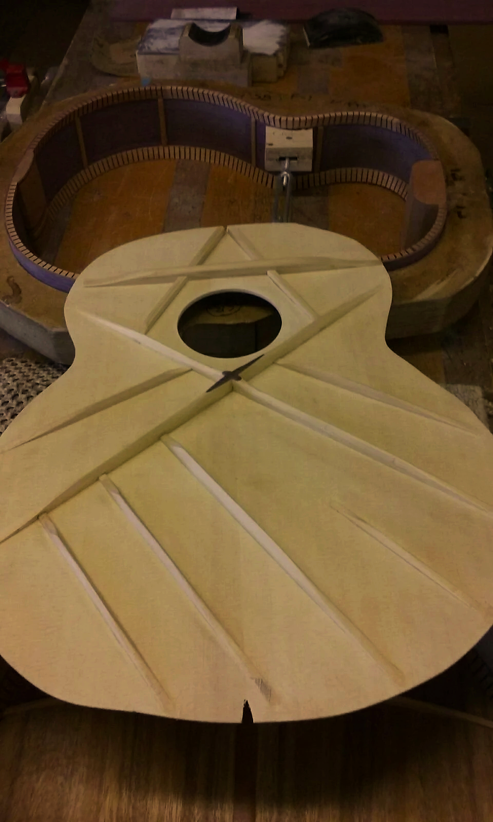 An unfinished wooden guitar body with an archtop design, placed on a worktable in a woodworking shop, with a guitar mold in the background.