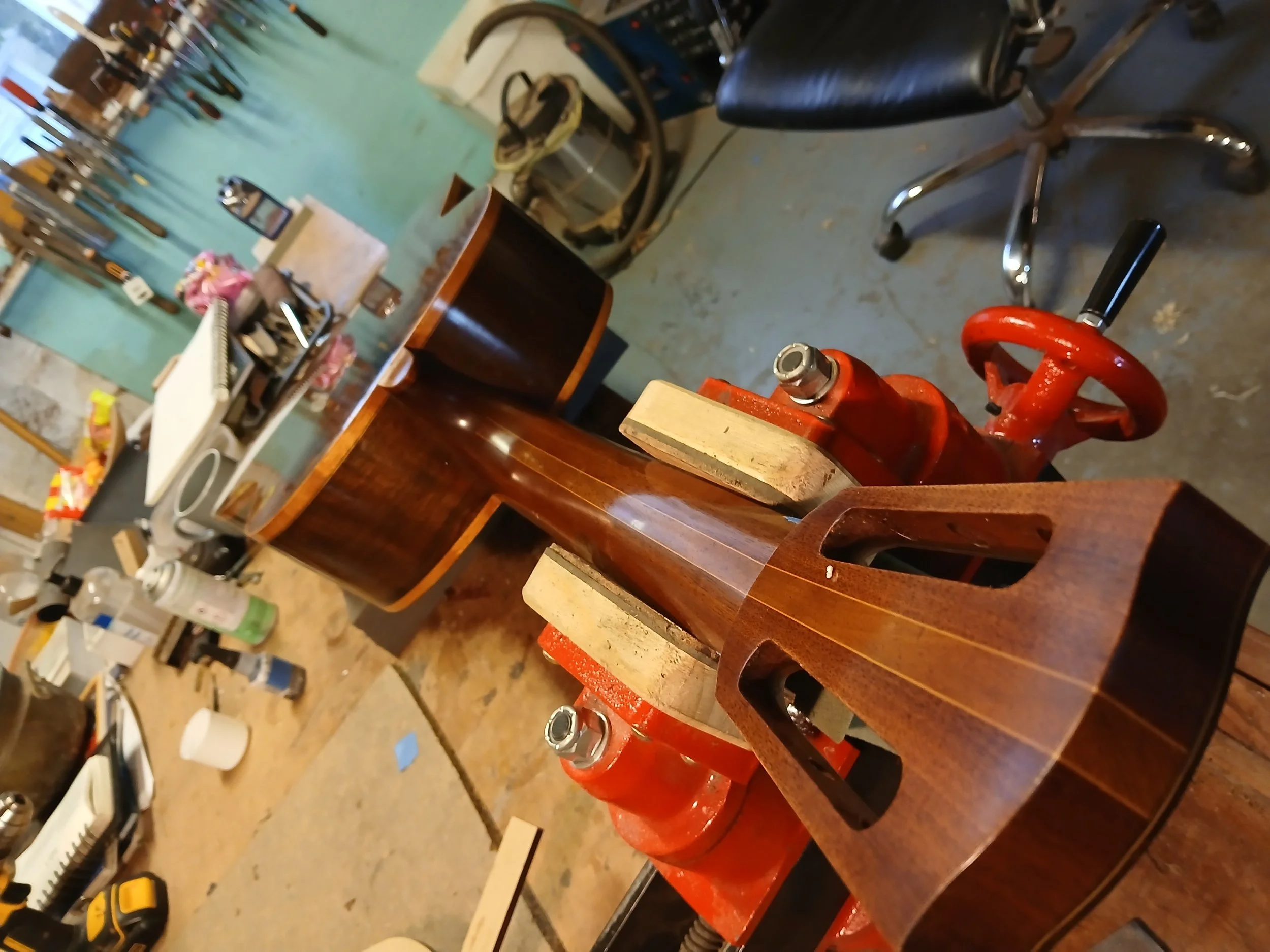 Close-up of a woodworking clamp holding a curved piece of dark wood on a workbench in a woodworking shop.