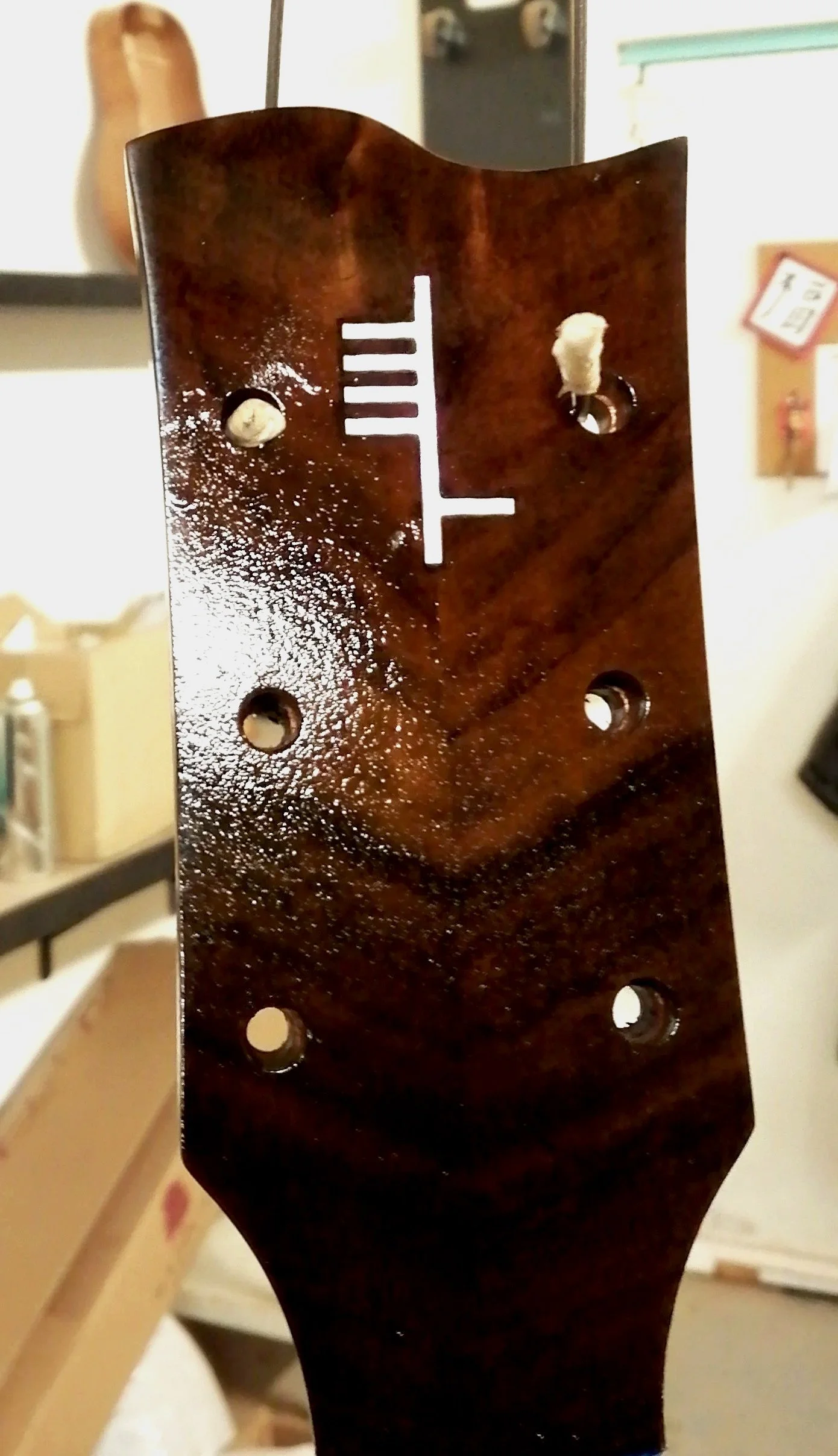 Close-up of the headstock of a guitar with a vintage finish and tuning pegs missing, showing four holes and a white fret marker.