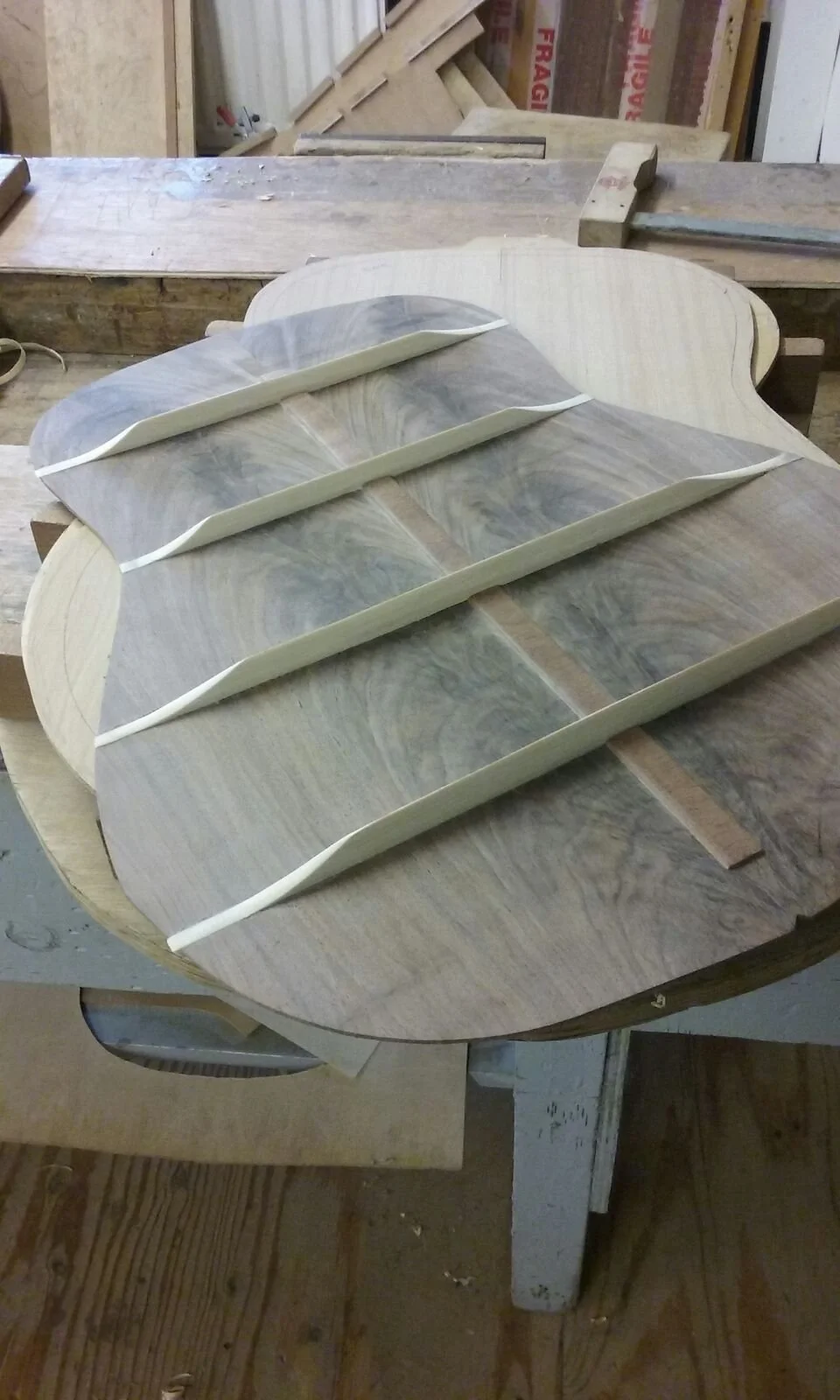 Wooden guitar body with inlaid wood pieces in a workshop, with tools nearby.
