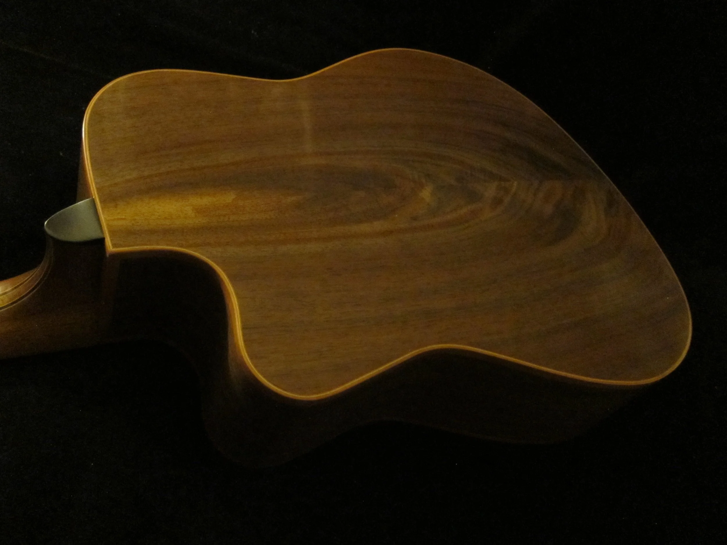 Back of a wooden ukulele against a black background.