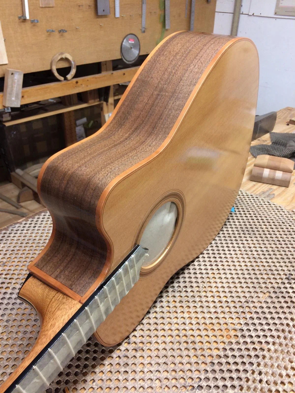 Close-up of a partially assembled acoustic guitar with a wooden body, showing the sound hole and the neck attached, in a woodworking shop.