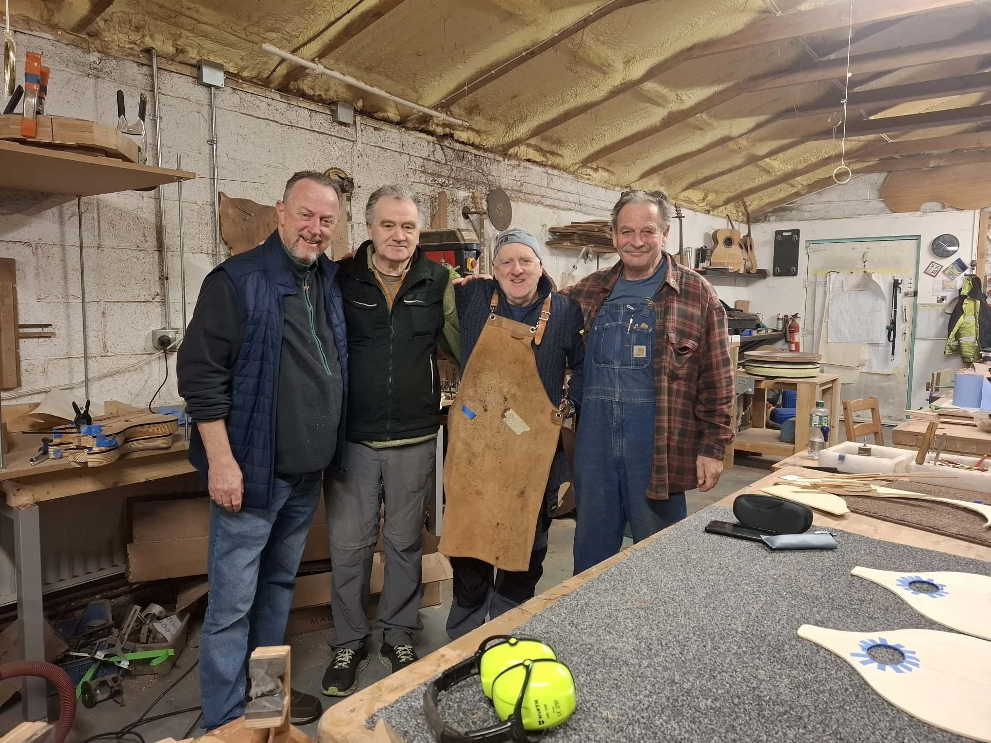 Four men standing together in a woodworking workshop, smiling and posing for the photo.