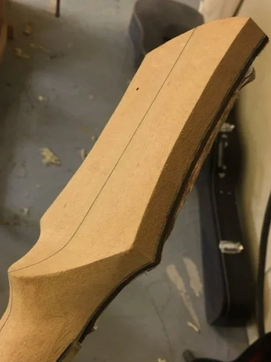 Close-up of a wooden guitar neck in a workshop, with lines and markings for construction.
