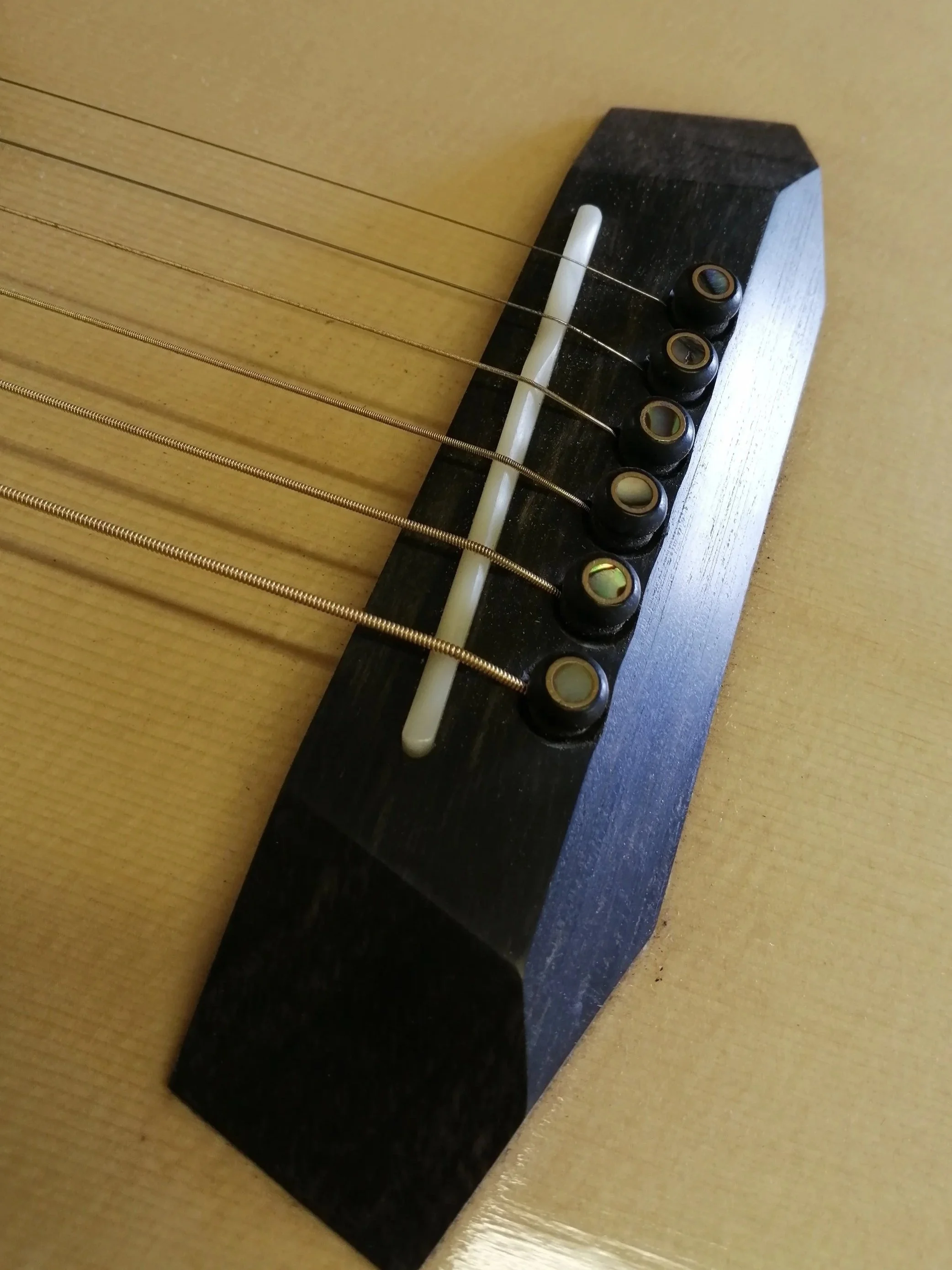Close-up of the bridge and saddle of an acoustic guitar showing strings and tuning pegs.