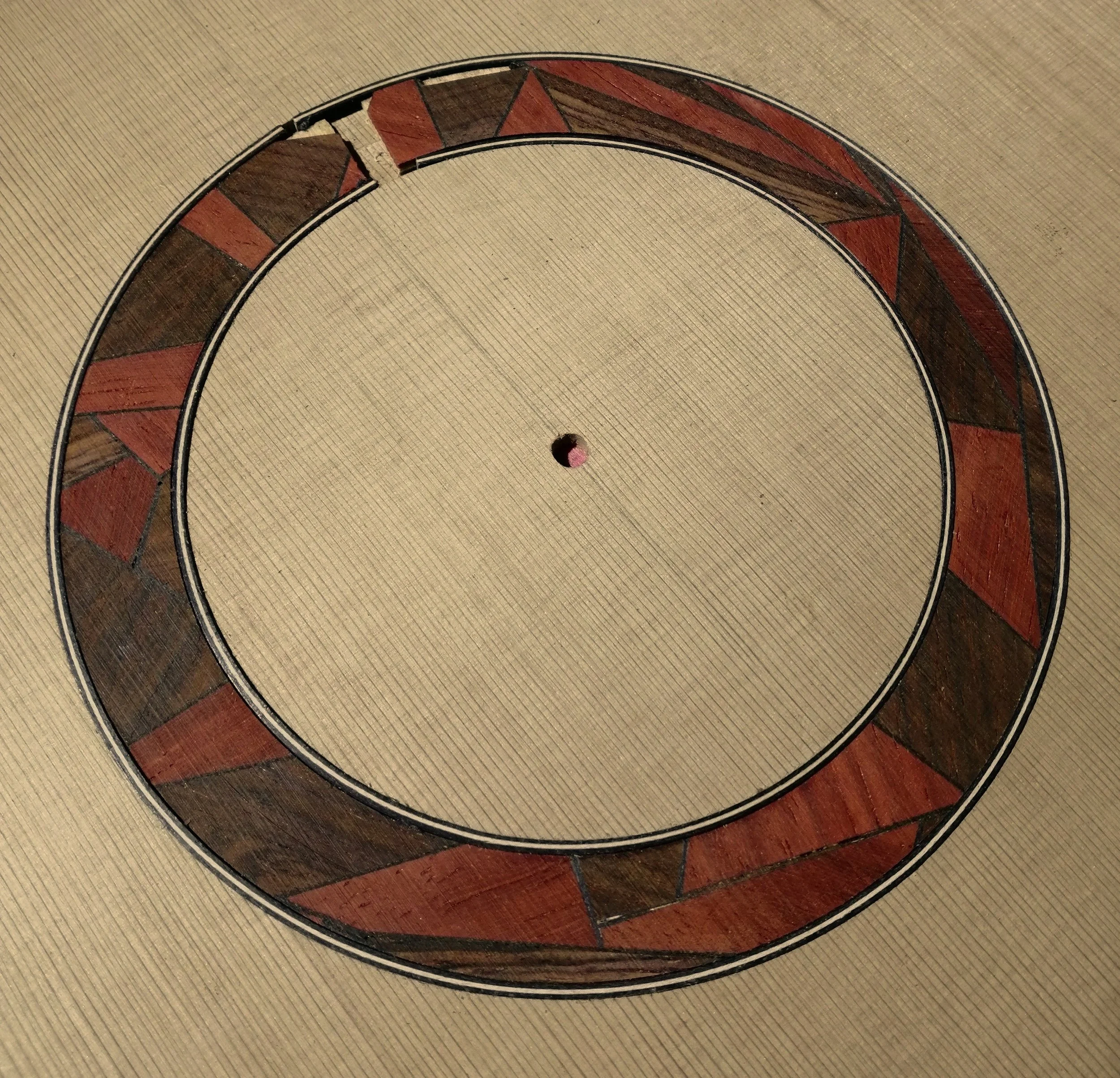 Close-up of a circular decorative piece on a beige woven surface, featuring a pattern of red and brown triangles.