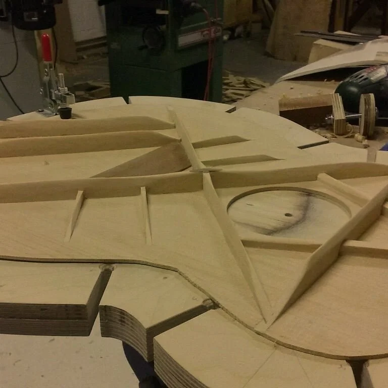 Wooden frame of a cello under construction on a workbench in a workshop.