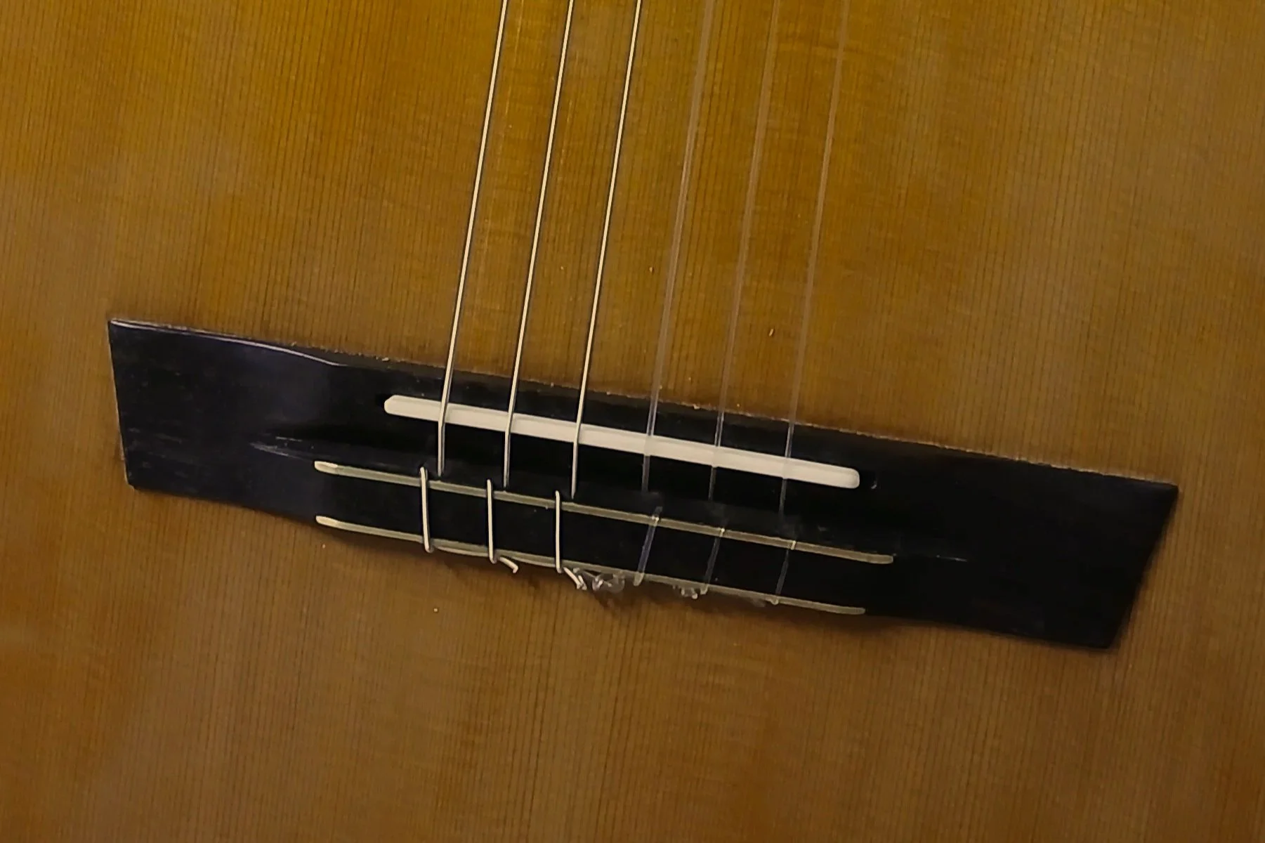 Close-up of a guitar bridge with strings on a wooden acoustic guitar.