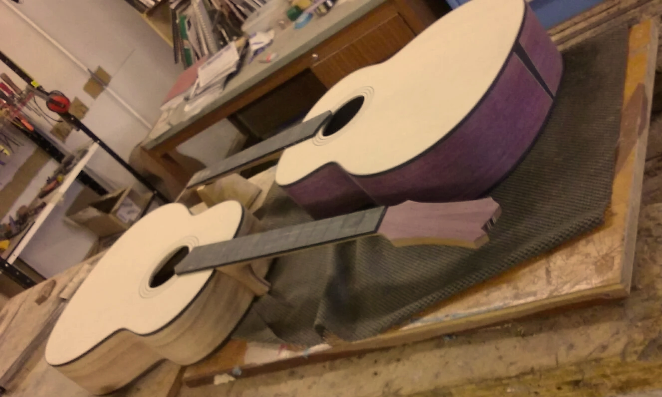 Two partially assembled acoustic guitars on a workbench in a workshop.
