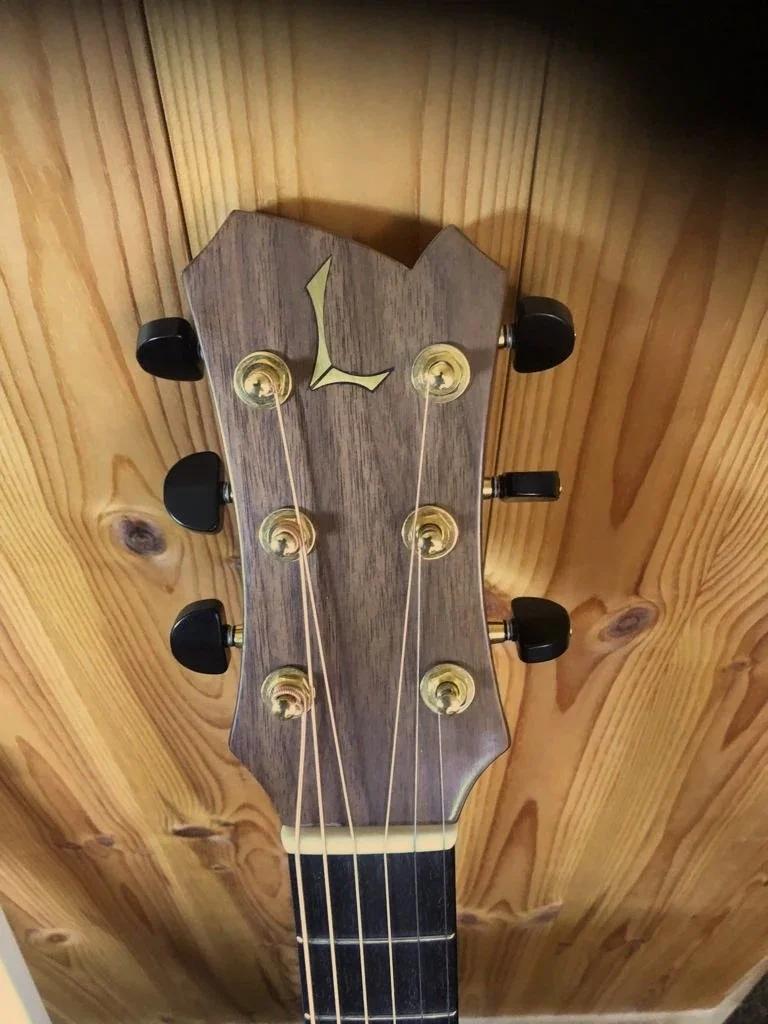 Close-up of a guitar headstock with tuning pegs on a wooden background.
