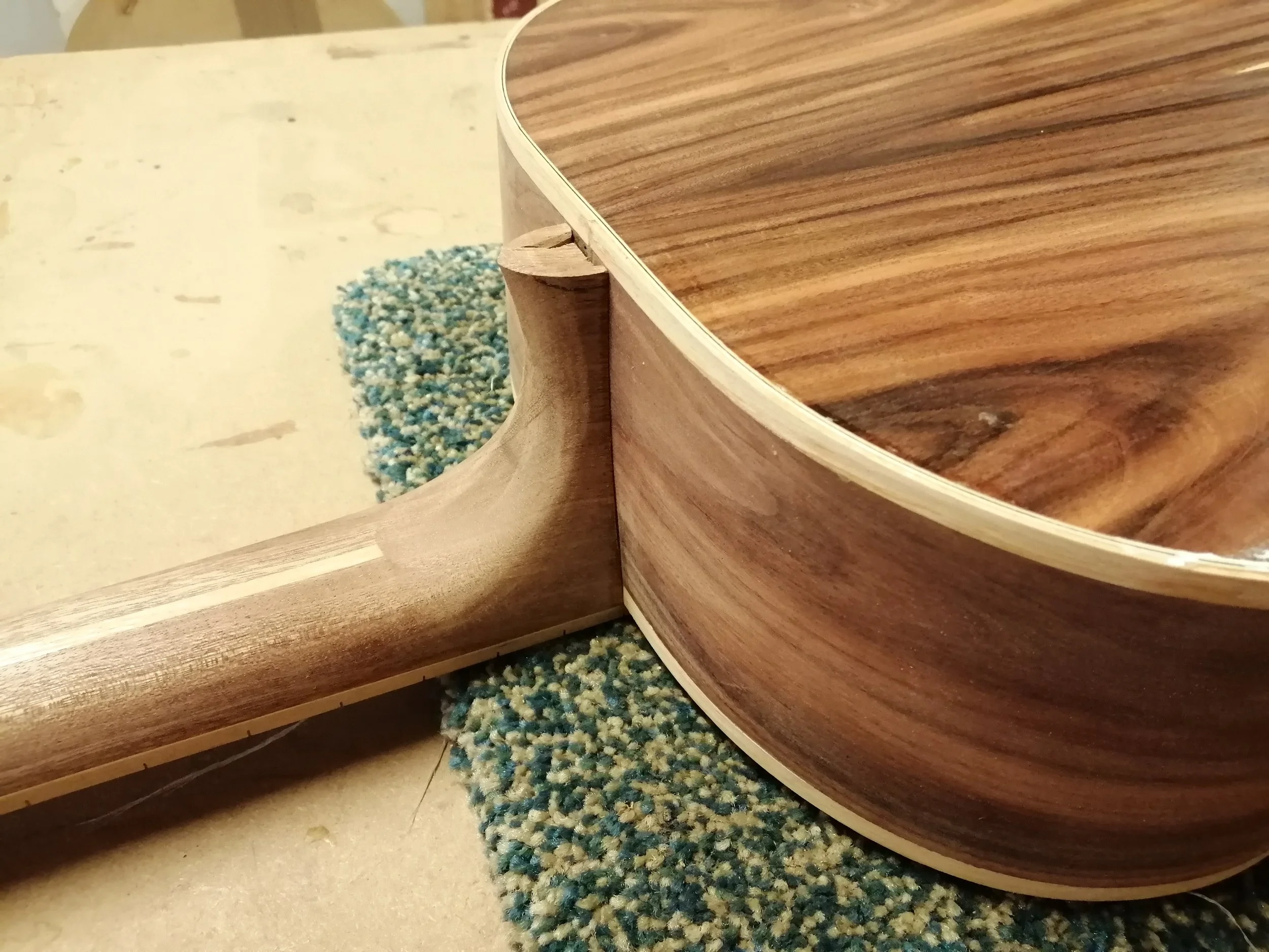 Close-up of a wooden guitar body and neck joint, showing the edge and joint detail.