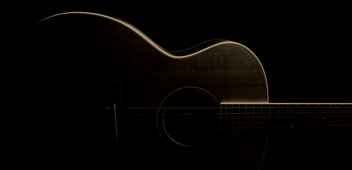 A dark, silhouetted acoustic guitar against a black background.
