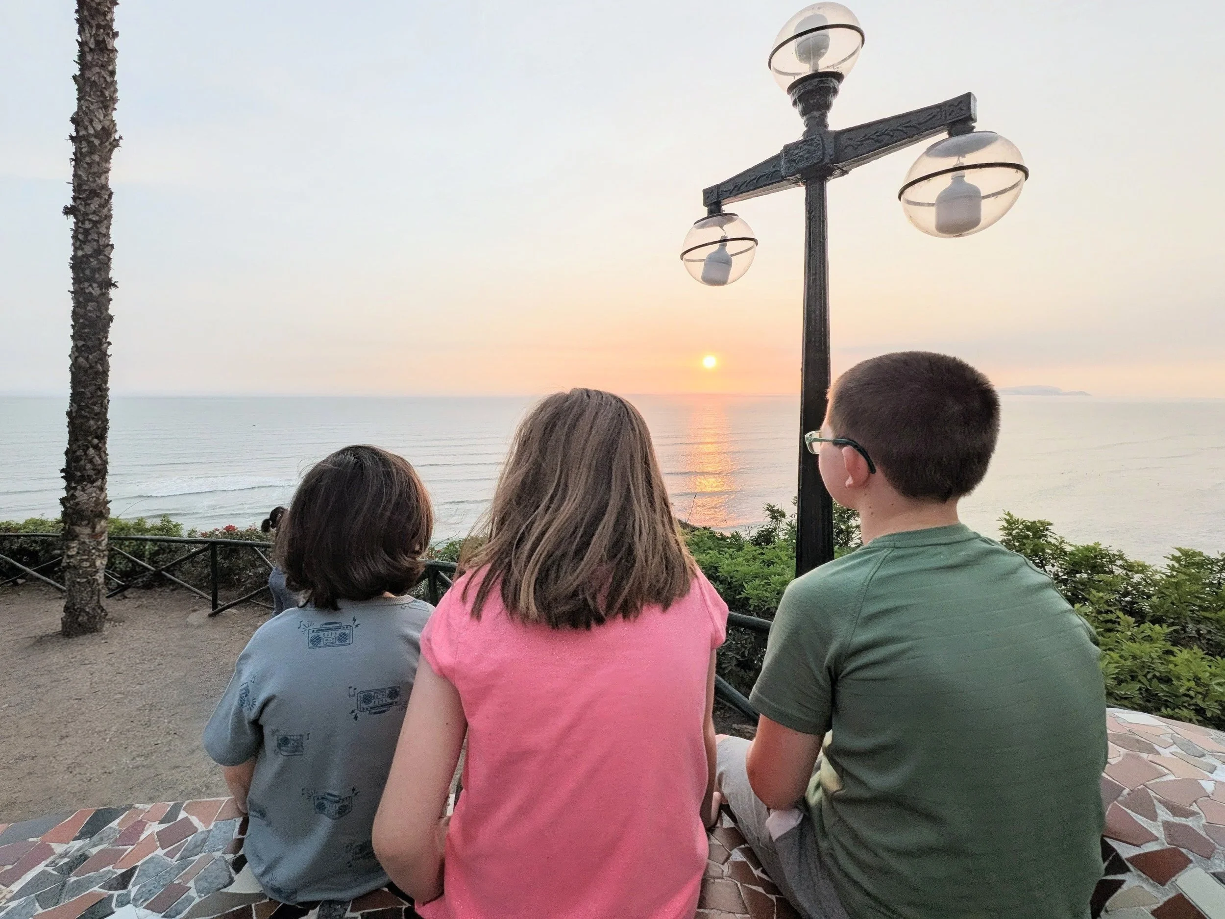 Three kids looking at the sunset over the Pacific Ocean in Lima, Peru.