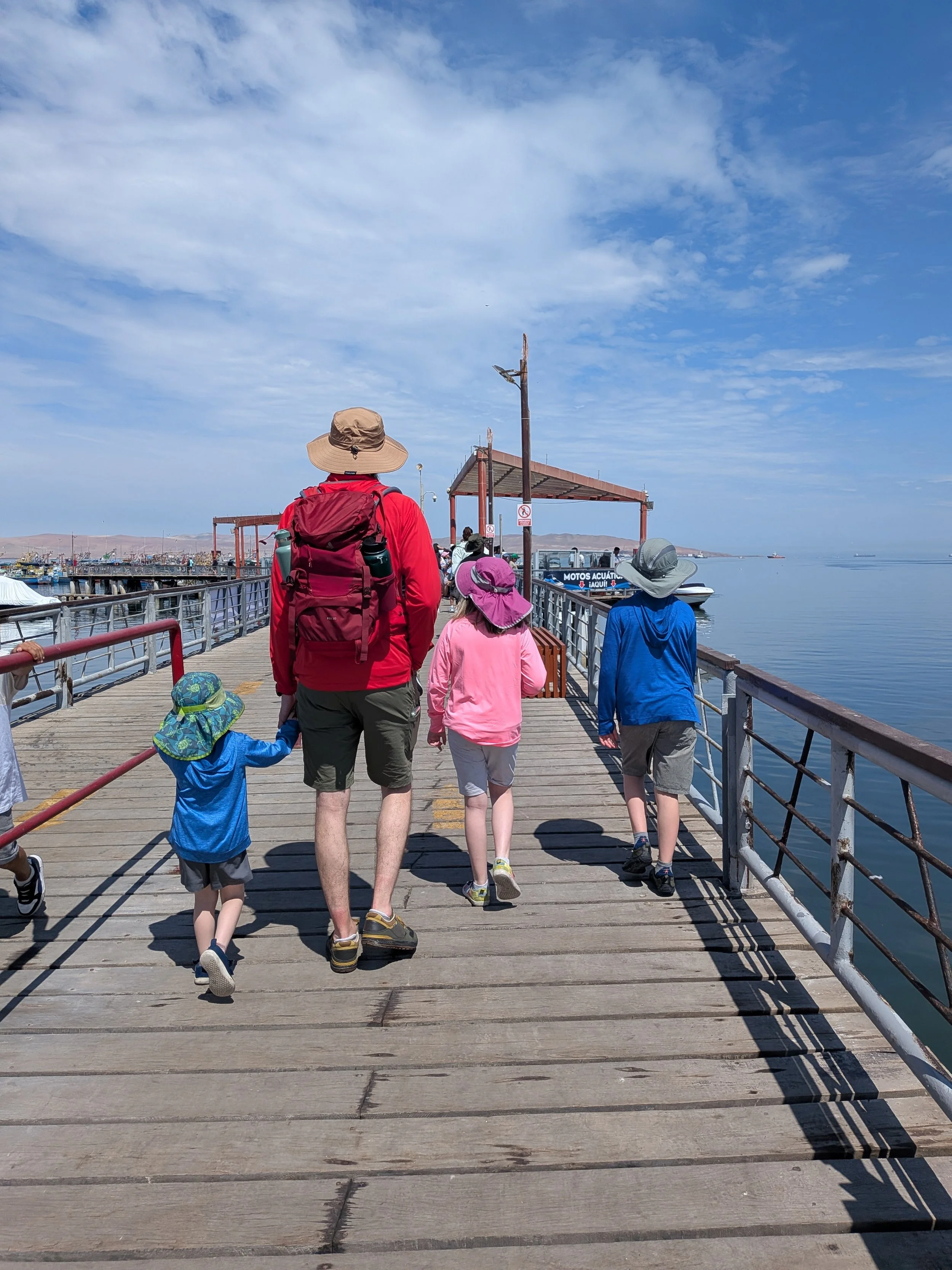 Dad and three kids, viewed from behind, as they walk down a pier.