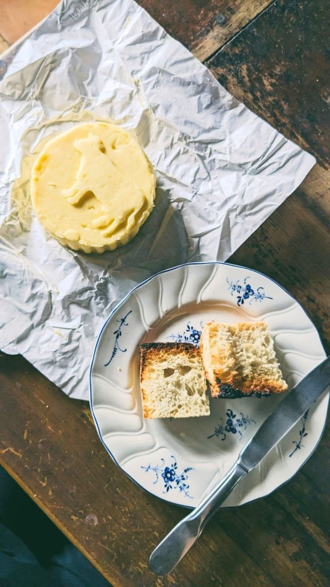 A serving of mashed potatoes on crinkled aluminum foil and slices of toasted bread with a knife on a blue and white floral plate, all on a wooden table.