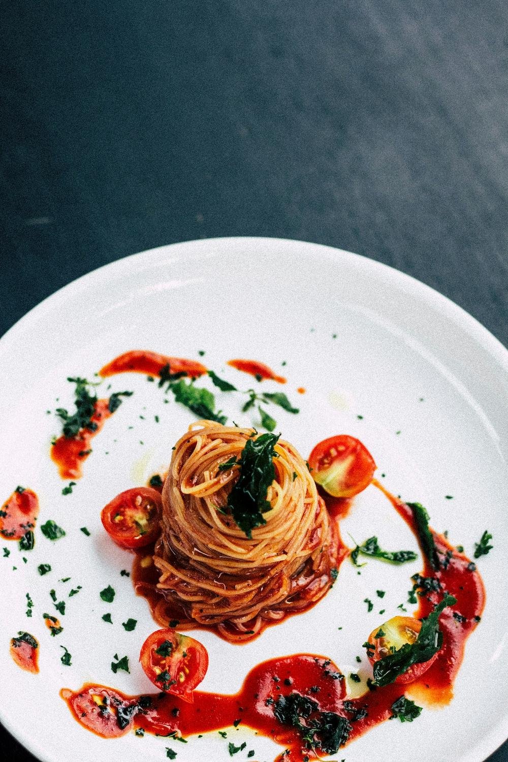 A plate of spaghetti garnished with cherry tomatoes, basil, and sauce, arranged in an elegant presentation.