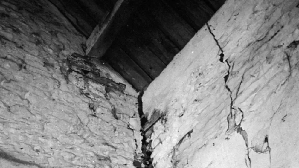 Close-up of a cracked and damaged brick wall in an old building, with a wooden roof above.