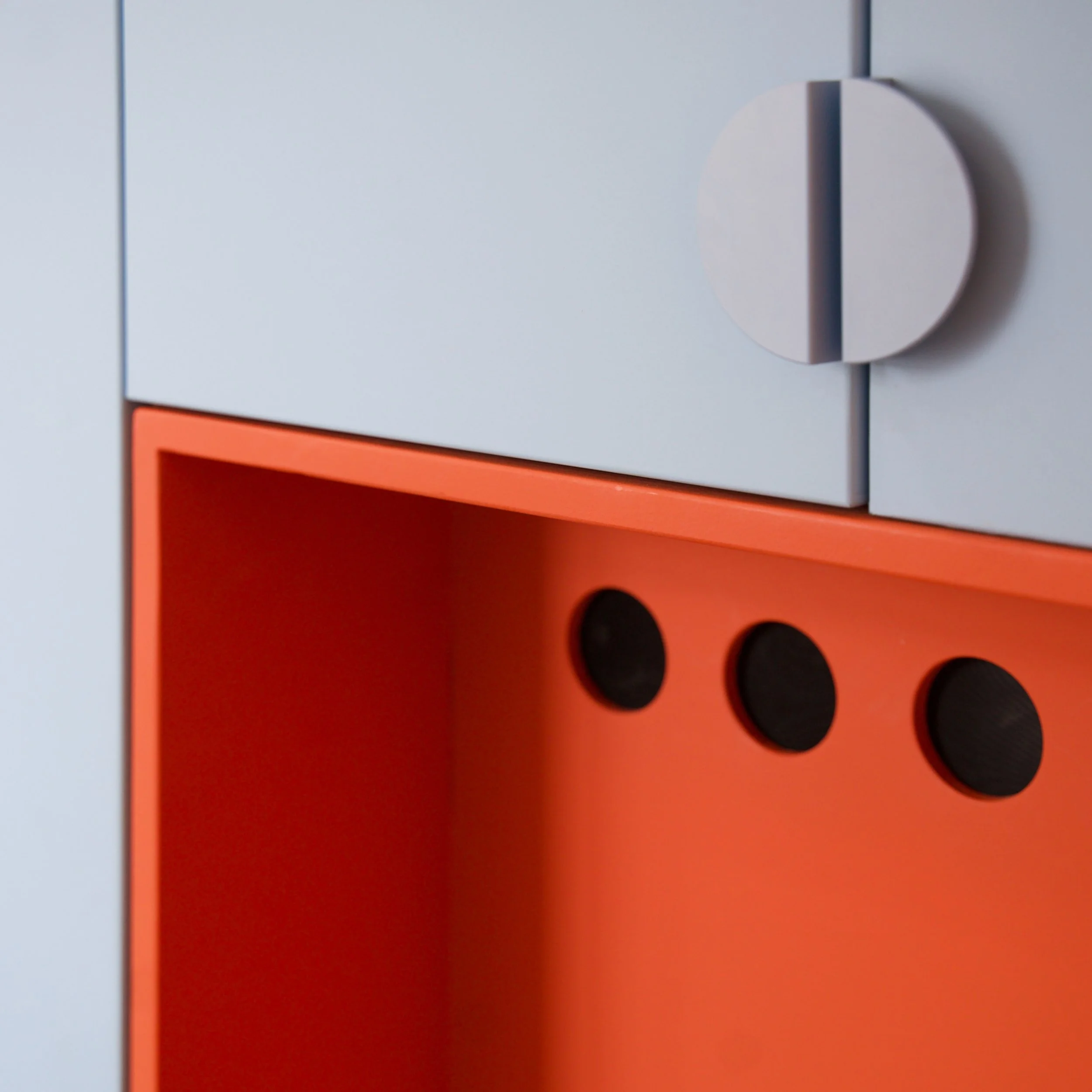 Close-up of a light blue and orange storage cabinet with round handles, with the focus on the door handle and the orange section of the cabinet.