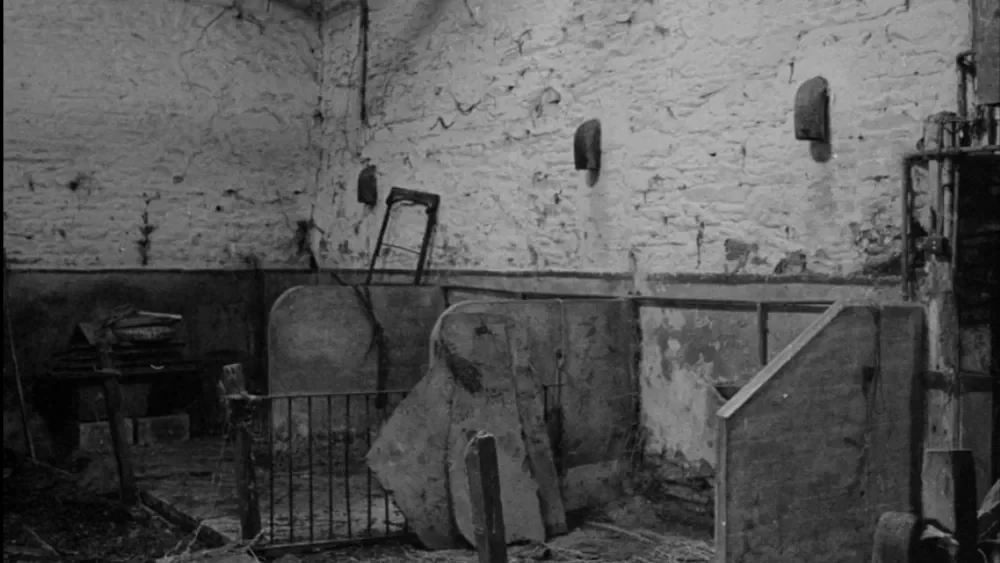 A black and white photo of an abandoned, dilapidated room with broken furniture and exposed brick walls.