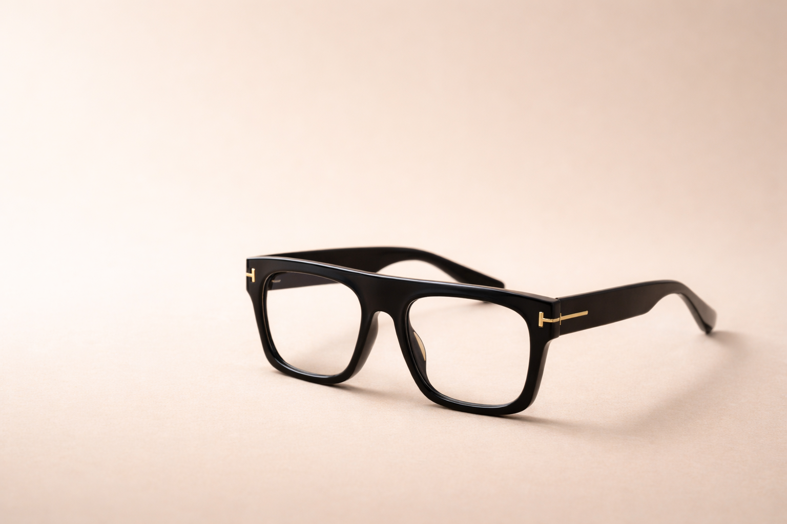 Black eyeglasses with gold accents on a neutral beige background.