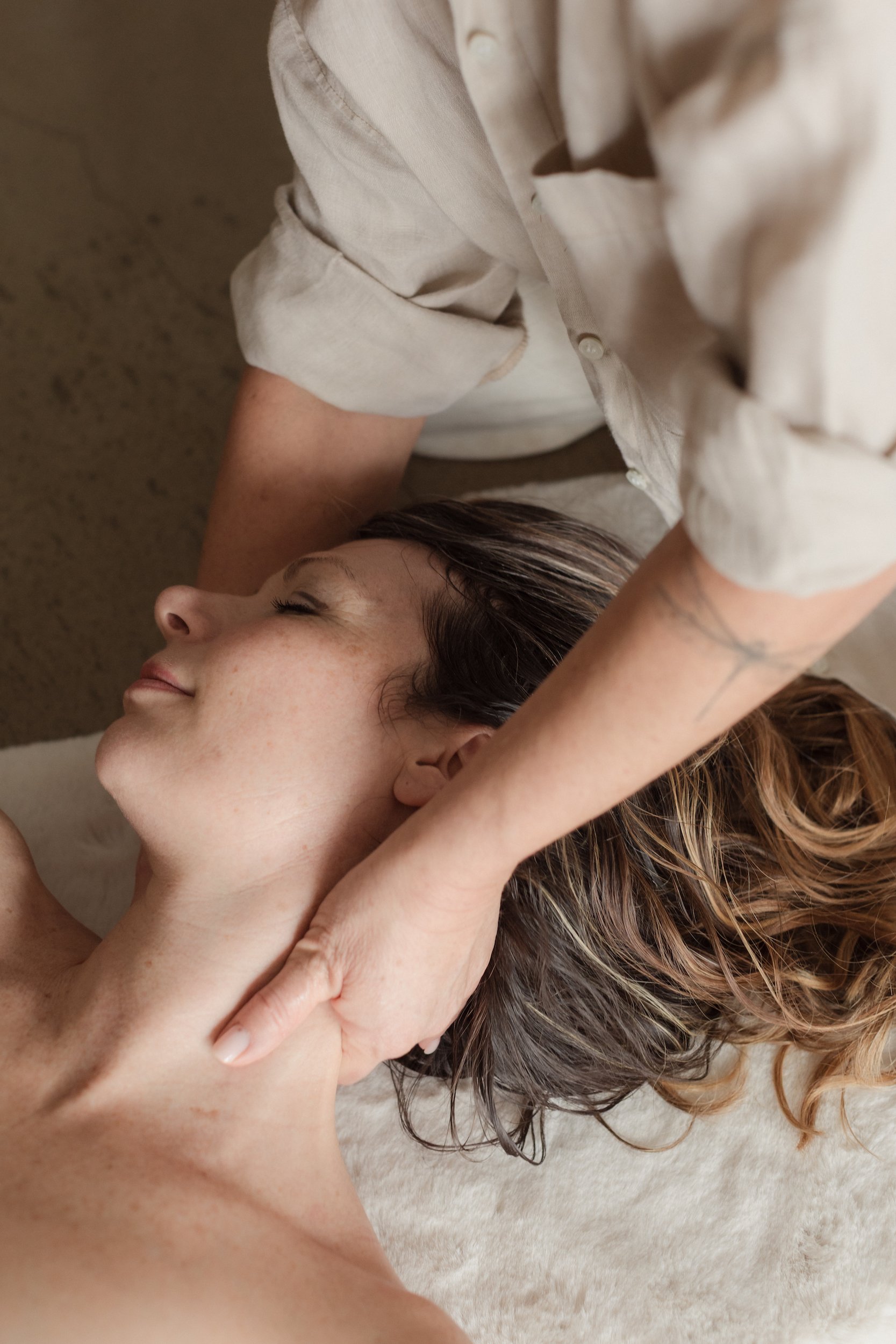 A woman with long, wavy brown hair lying on her back receiving a massage, with a calm expression on her face.