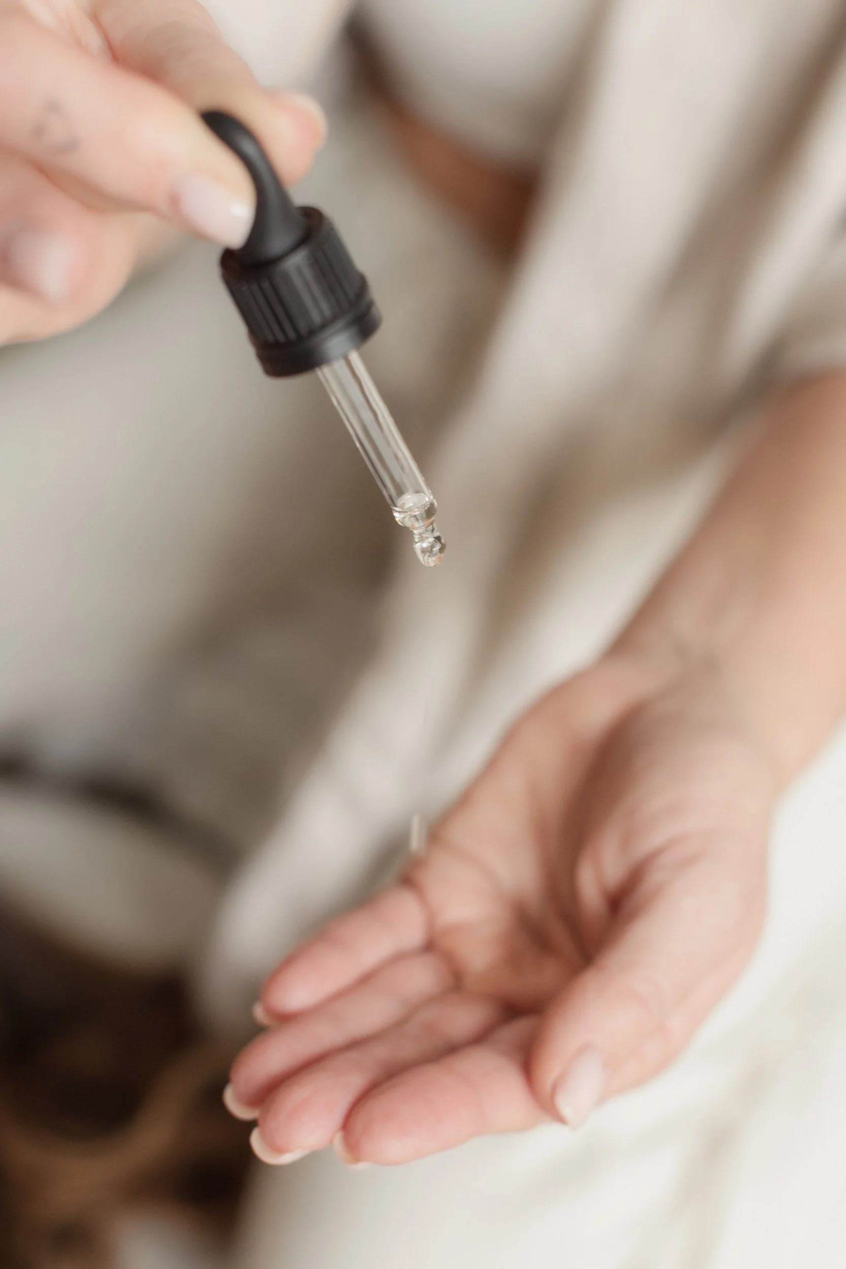 Close-up of a hand holding a dropper with a clear liquid, possibly administering medicine or eye drops, with a blurred background.