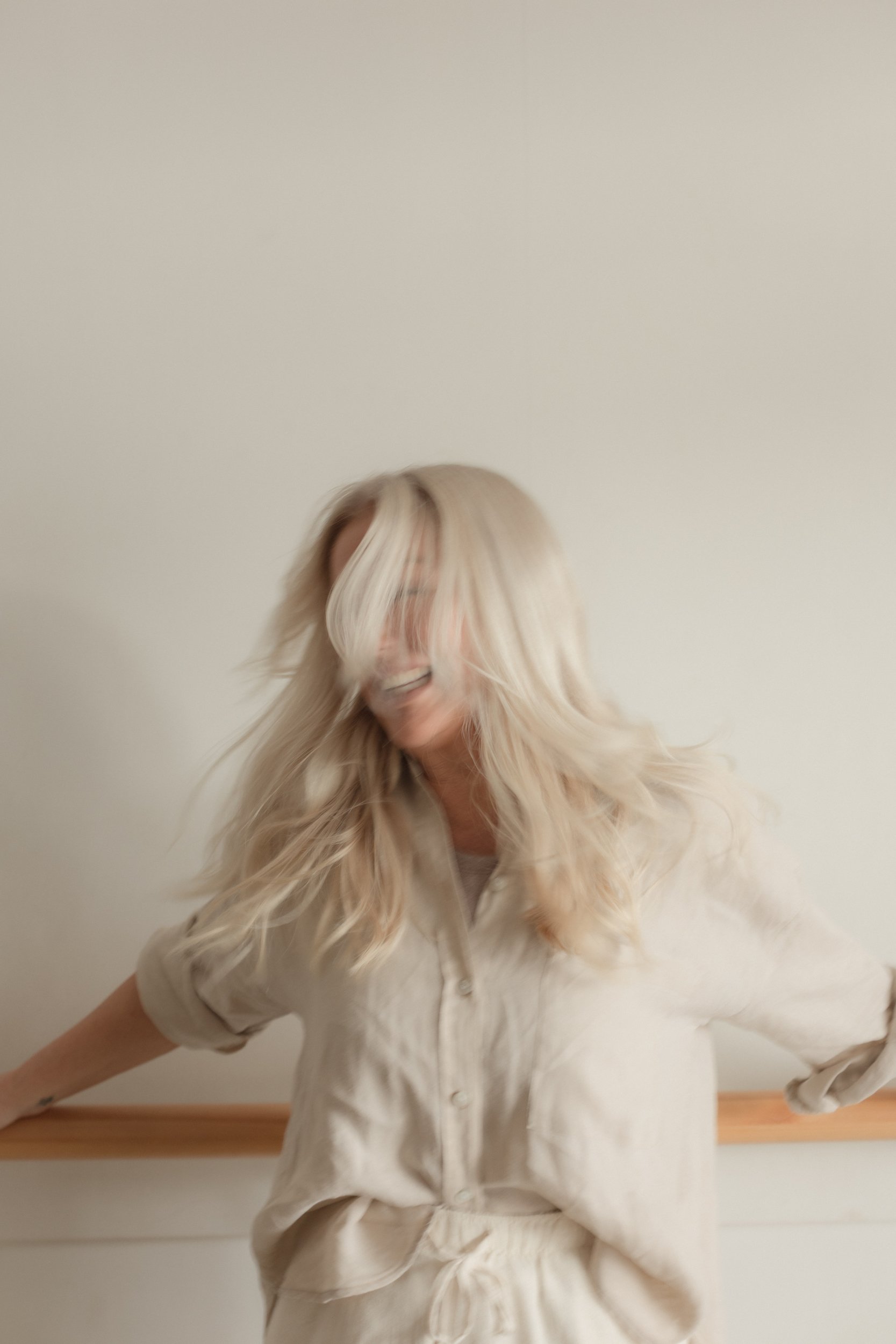Blonde lady dressed in neutrals leaning against studio bar