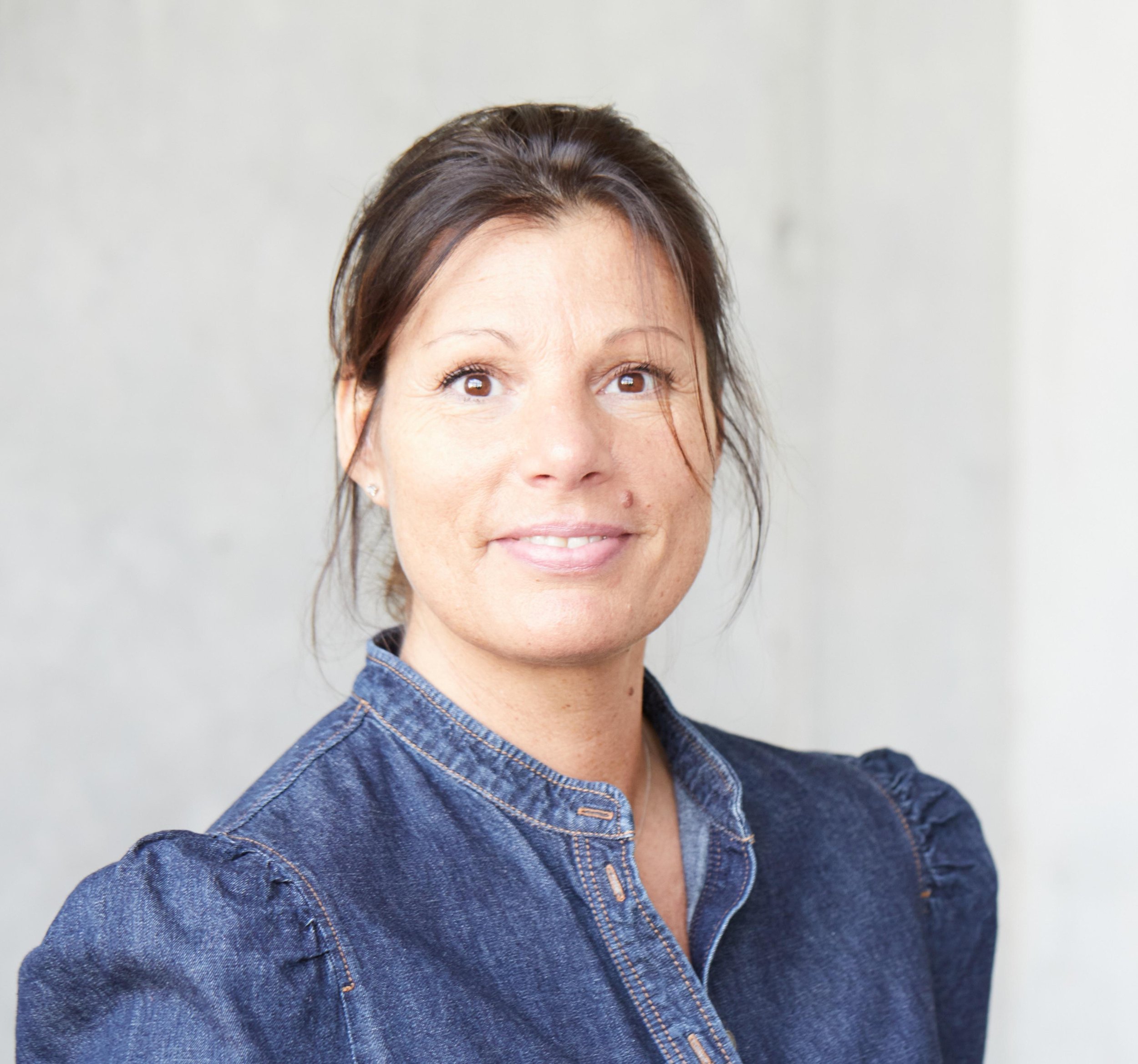 Nahaufnahme einer lächelnden Frau in Jeanshemd vor hellem Hintergrund.