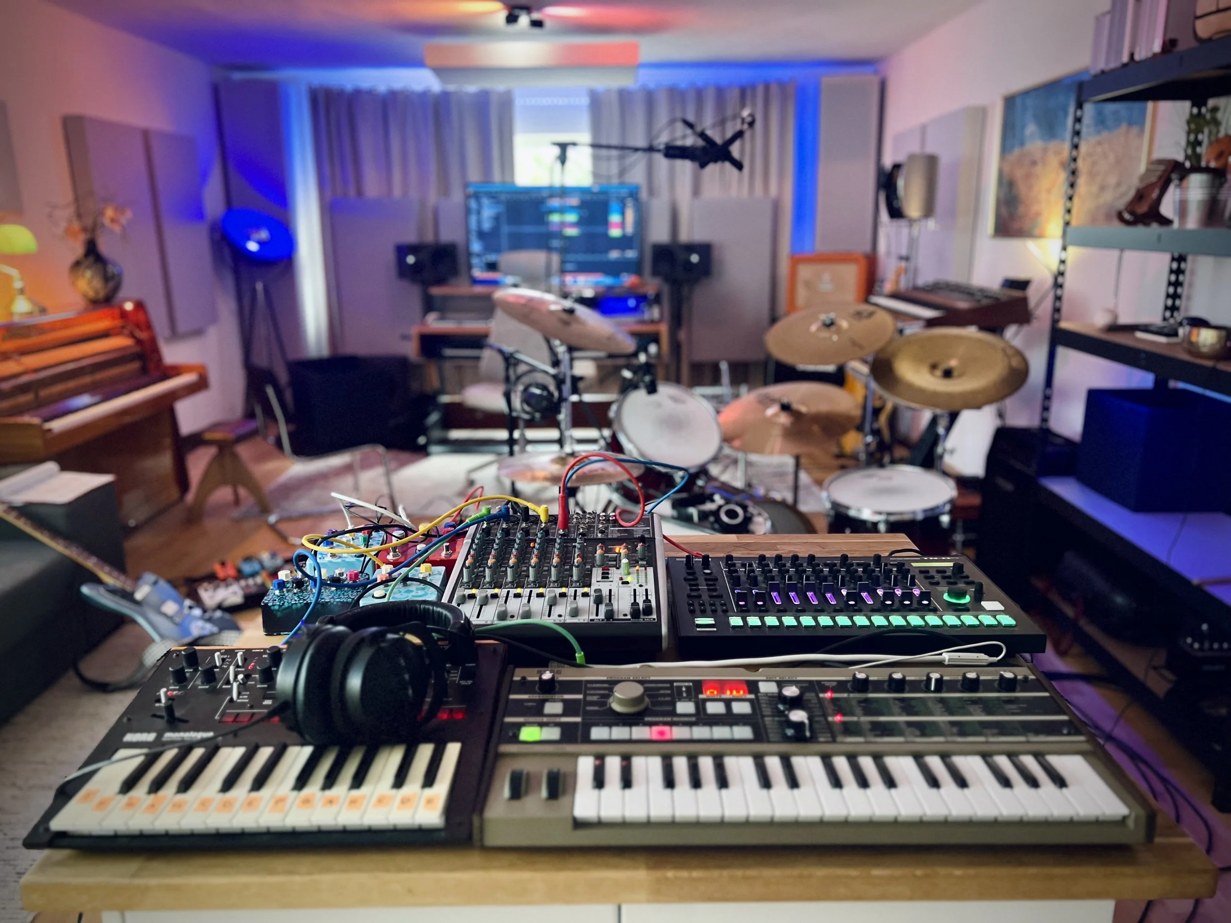 Musikstudio mit elektronischen Geräten, Schlagzeug, Klavier, Moderationspult und Requisiten für Musikproduktion und Studioaufnahme.