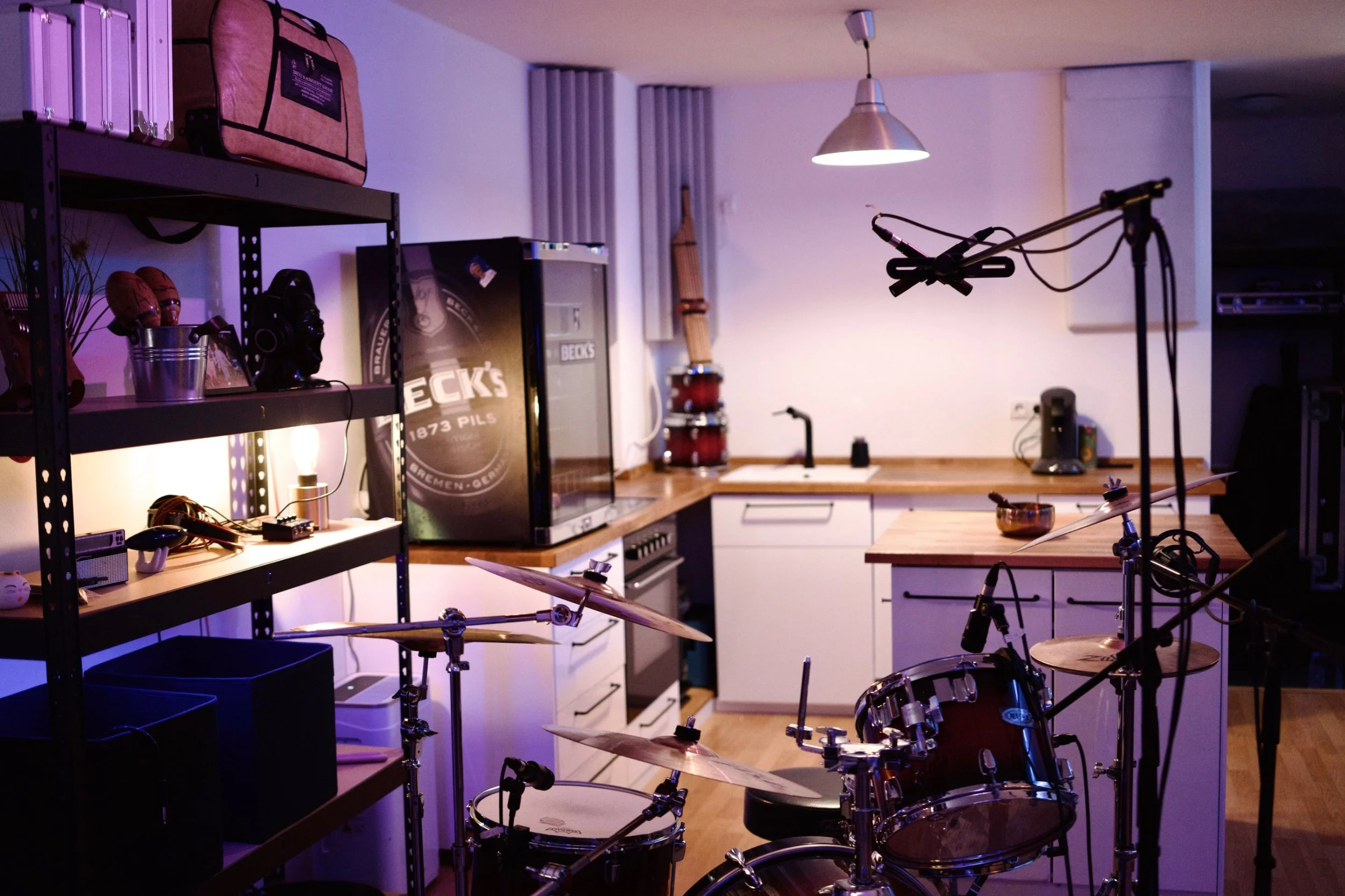 Ein Musikraum mit Schlagzeug, Gitarren, Mikrofon, Laptop, und Aufnahmeequipment, in einer modernen, gut ausgestatteten Einrichtung.