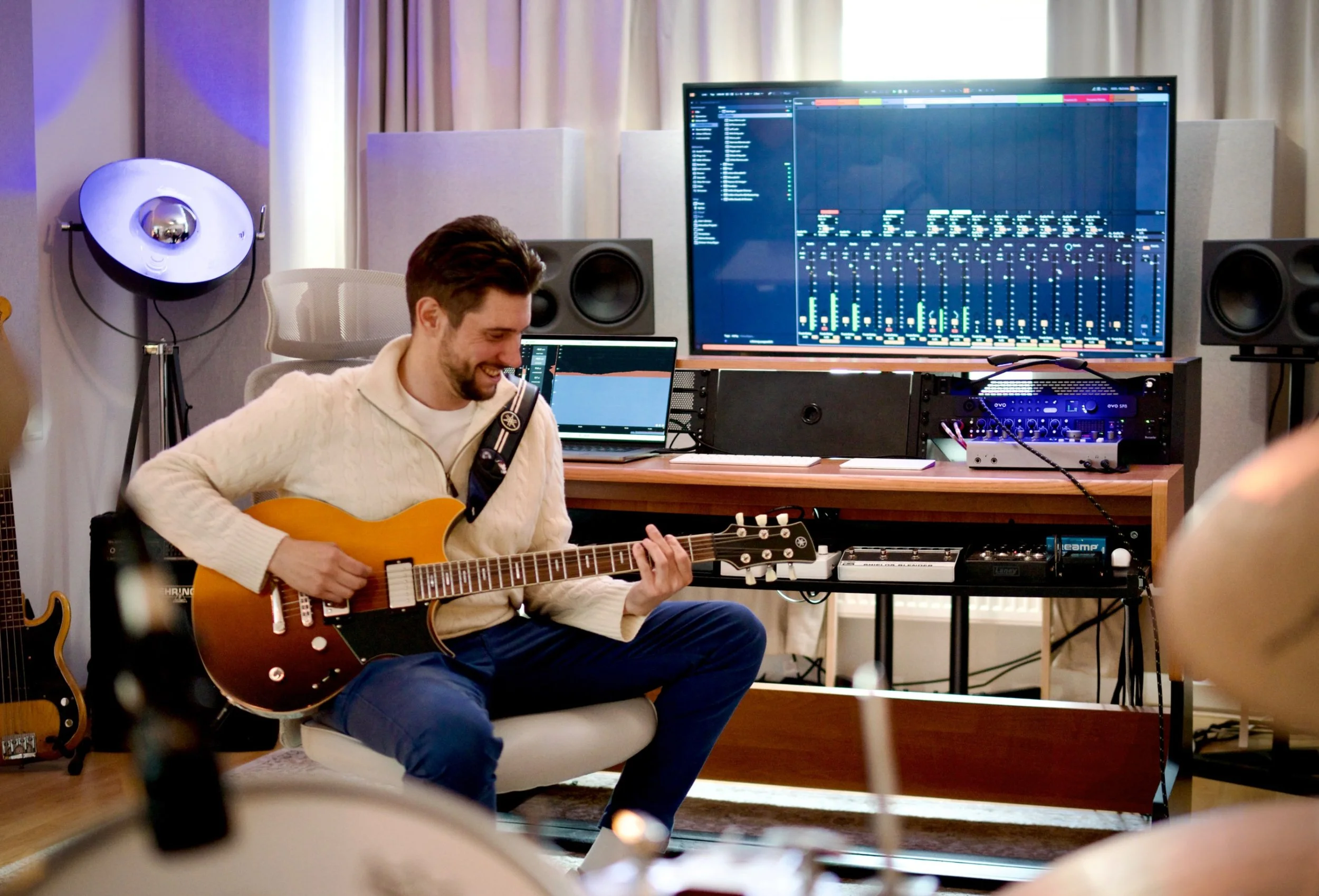 Ein Mann spielt Gitarre in einem Musikstudio, umgeben von Musikinstrumenten und Tontechnik.