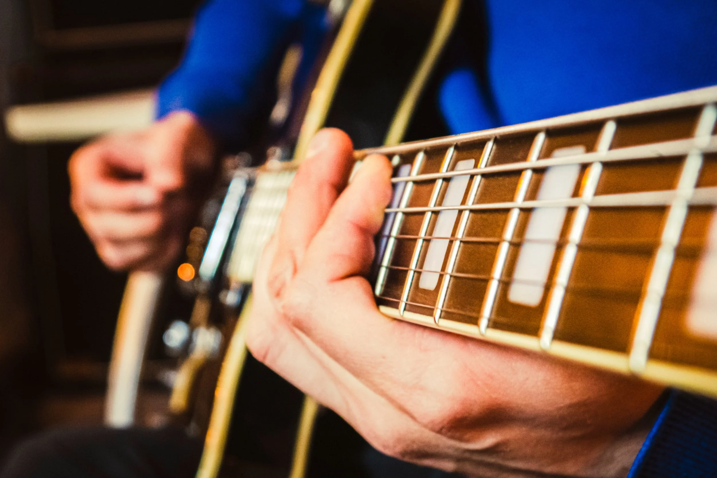 Eine Person spielt Gitarre, Nahaufnahme der Hand auf den Gitarrensaiten.