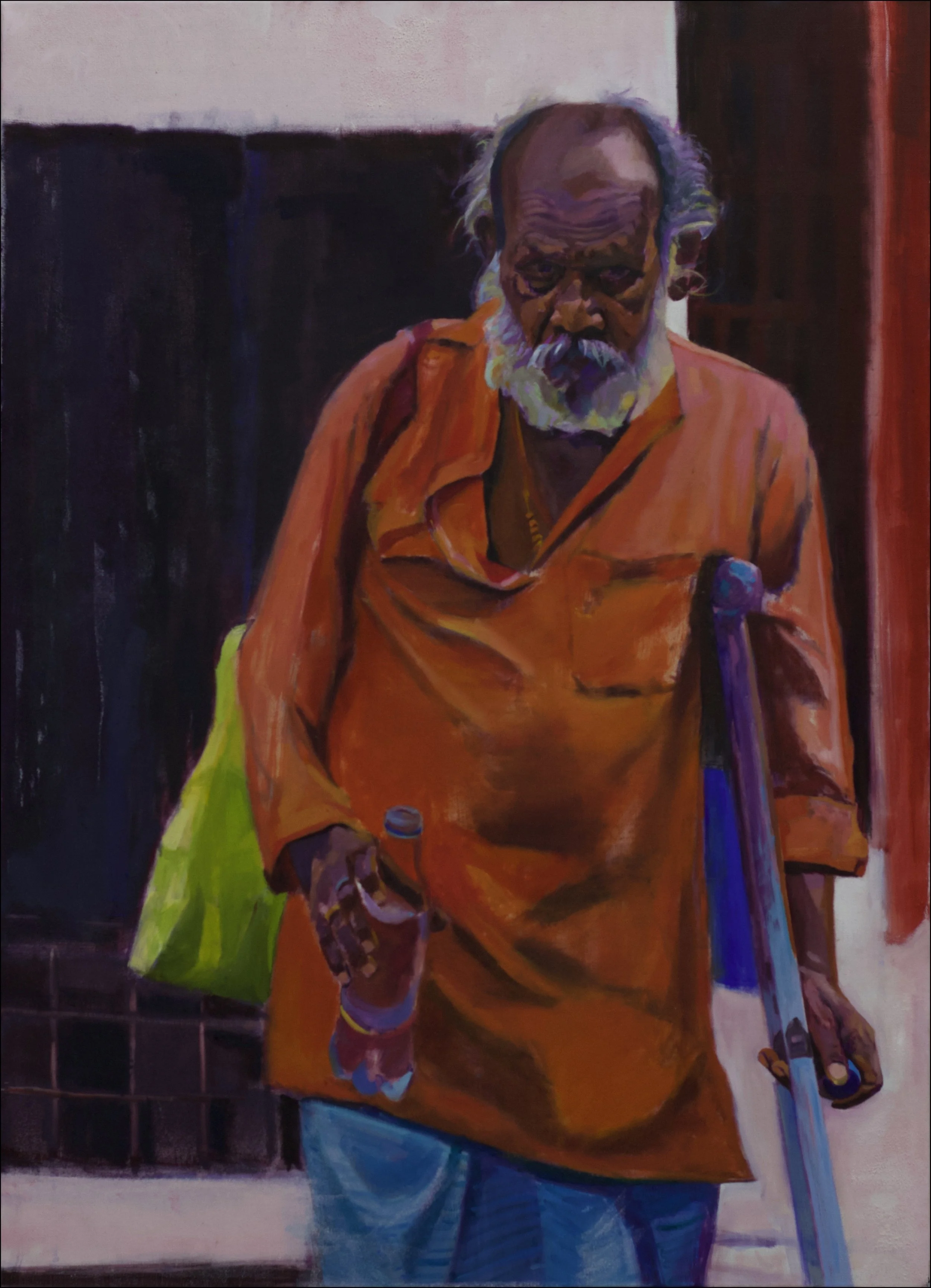 An Indian man with a white beard, wearing an orange shirt, holding a water bottle in his left hand, walking on the street.