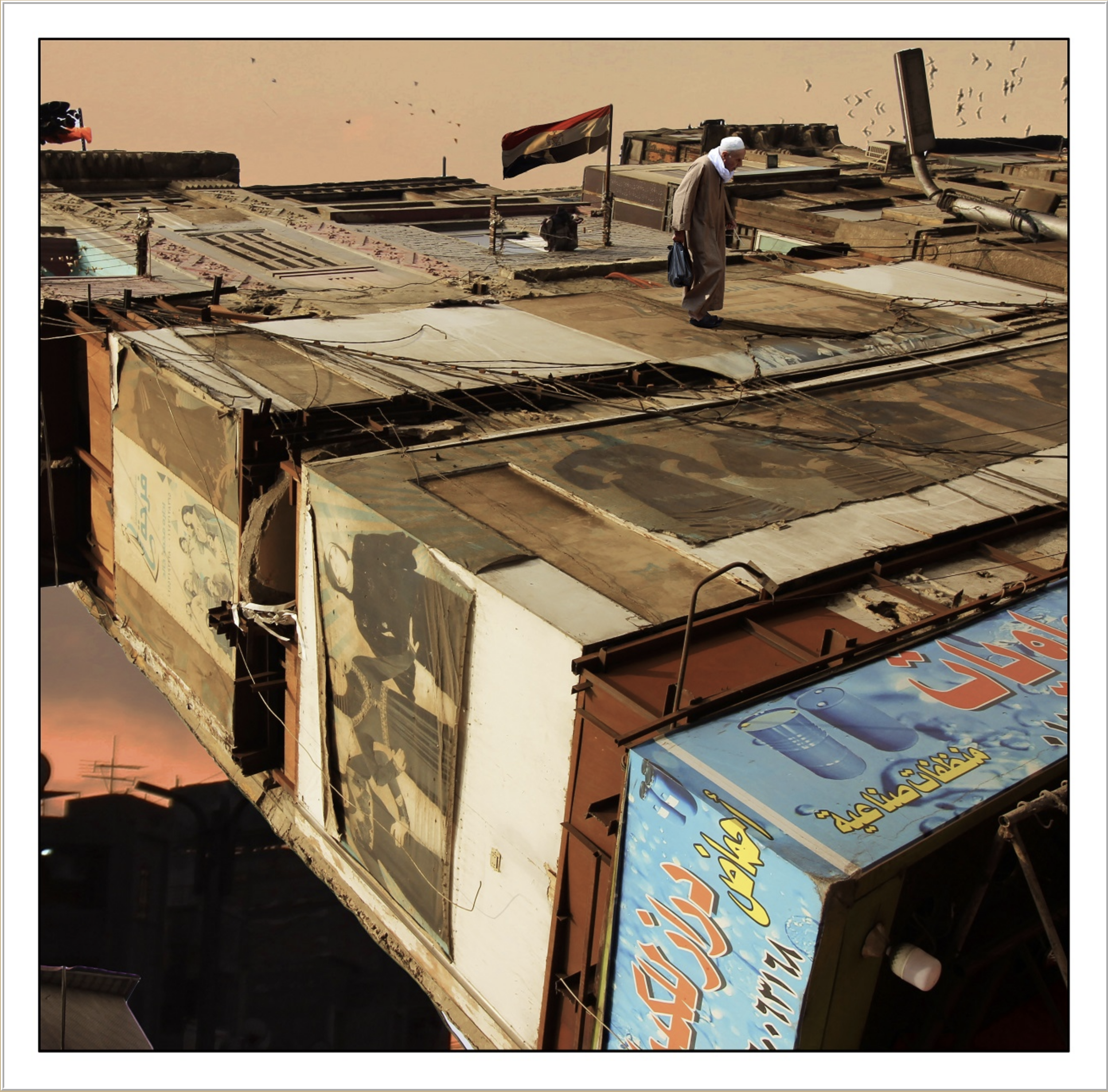 A man walking on a rooftop with a flag and a flock of birds in the sky during sunset.