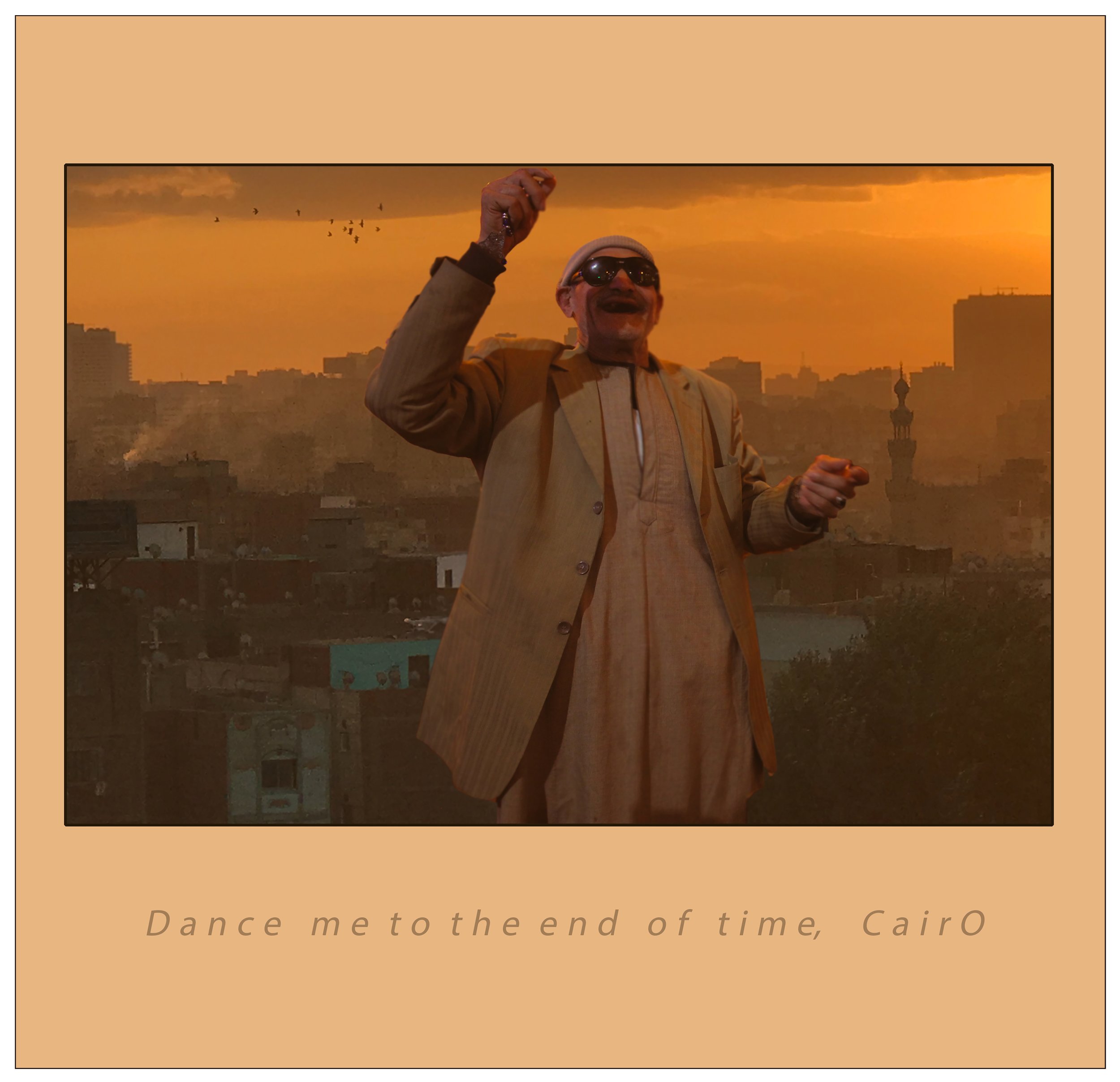 A man in a beige suit and sunglasses holding a small object while smiling at sunset cityscape in the background. The image has a warm orange tone. Text at the bottom reads, 'Dance me to the end of time, Cairo.'
