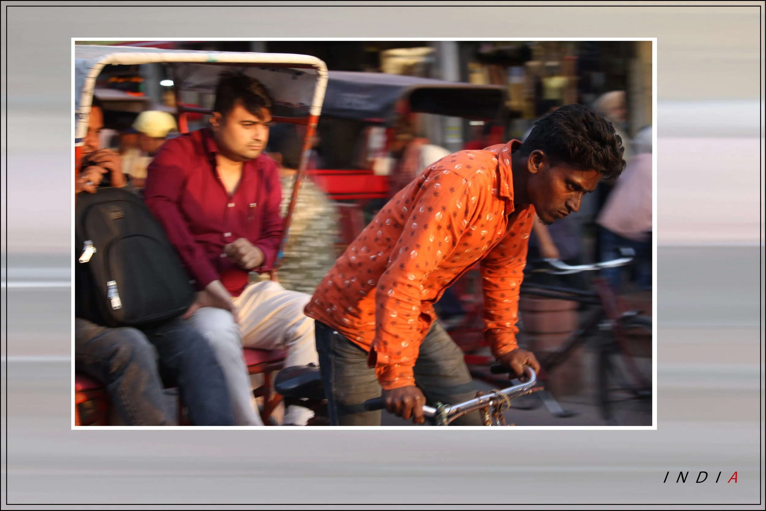 A man riding a bicycle with a person seated on the back, and other vehicles and pedestrians in the background in India.