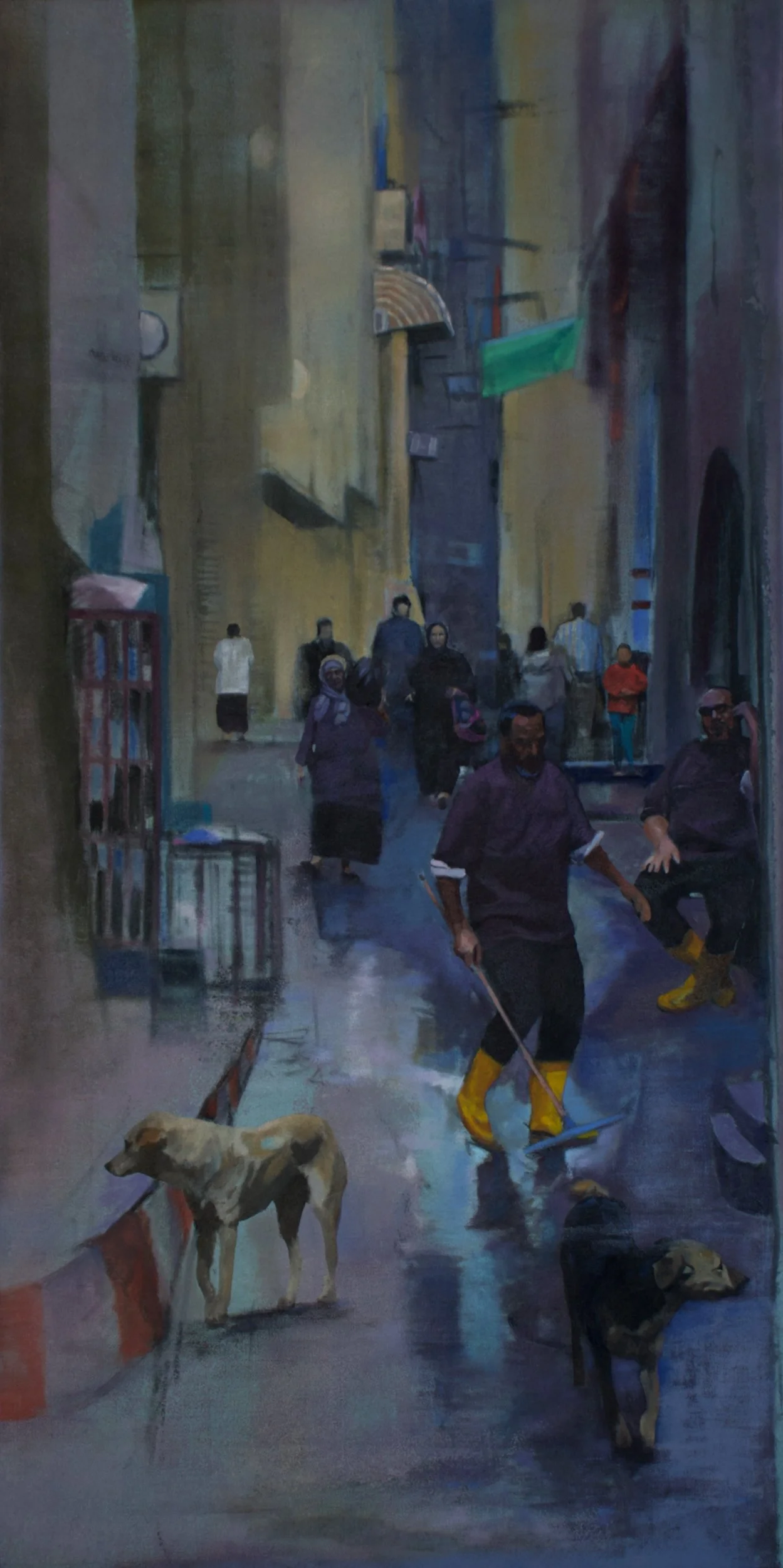A street scene in an urban area at dusk or early evening, with people walking and sitting. In the foreground, a person is sweeping the wet street with yellow boots, and two dogs are present, one visible in the foreground and another farther back. Buildings line both sides of the street, with various signs and awnings, and some individuals are wearing masks.