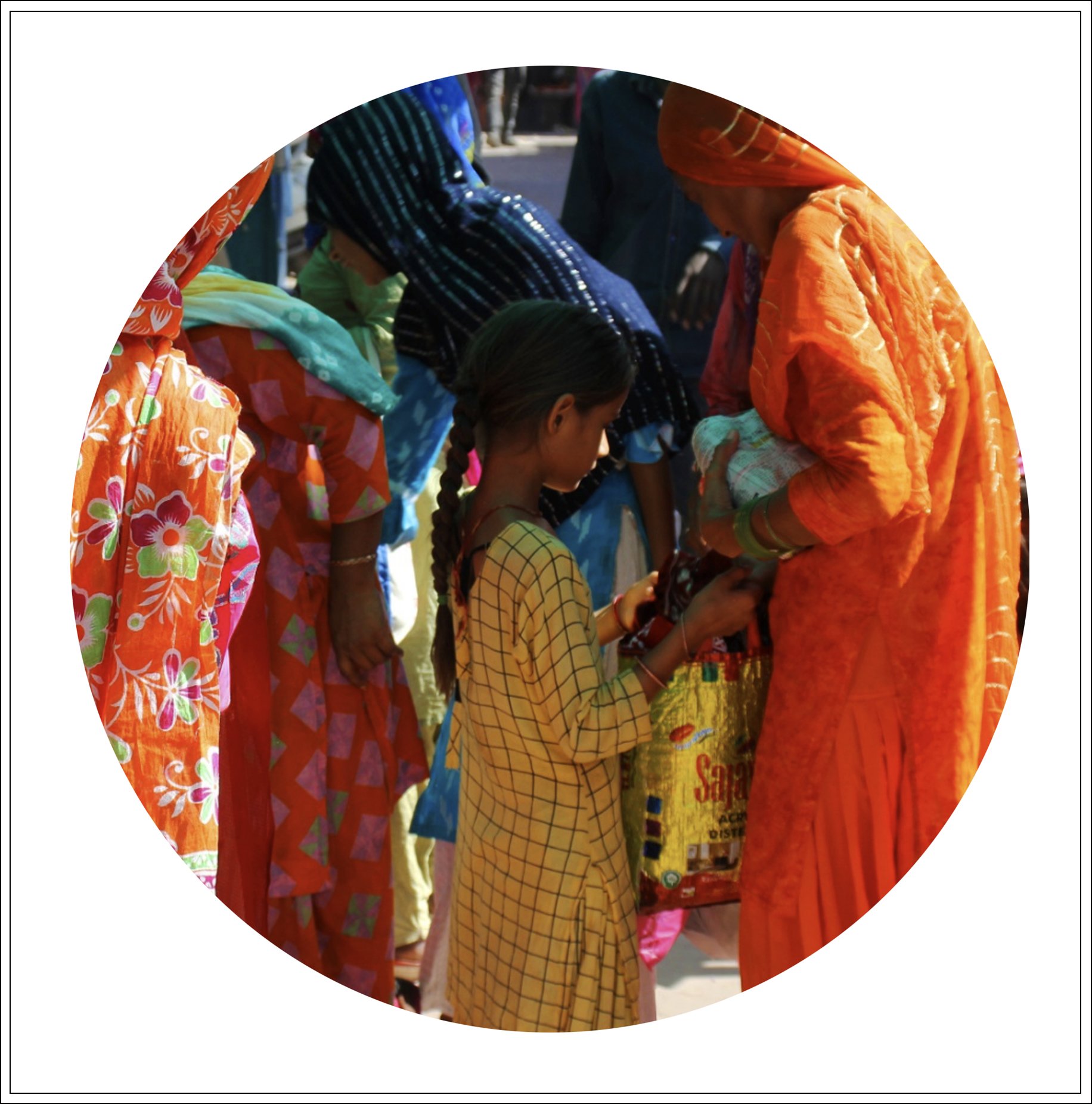 Children and women dressed in colorful traditional Indian clothing, gathered outdoors.