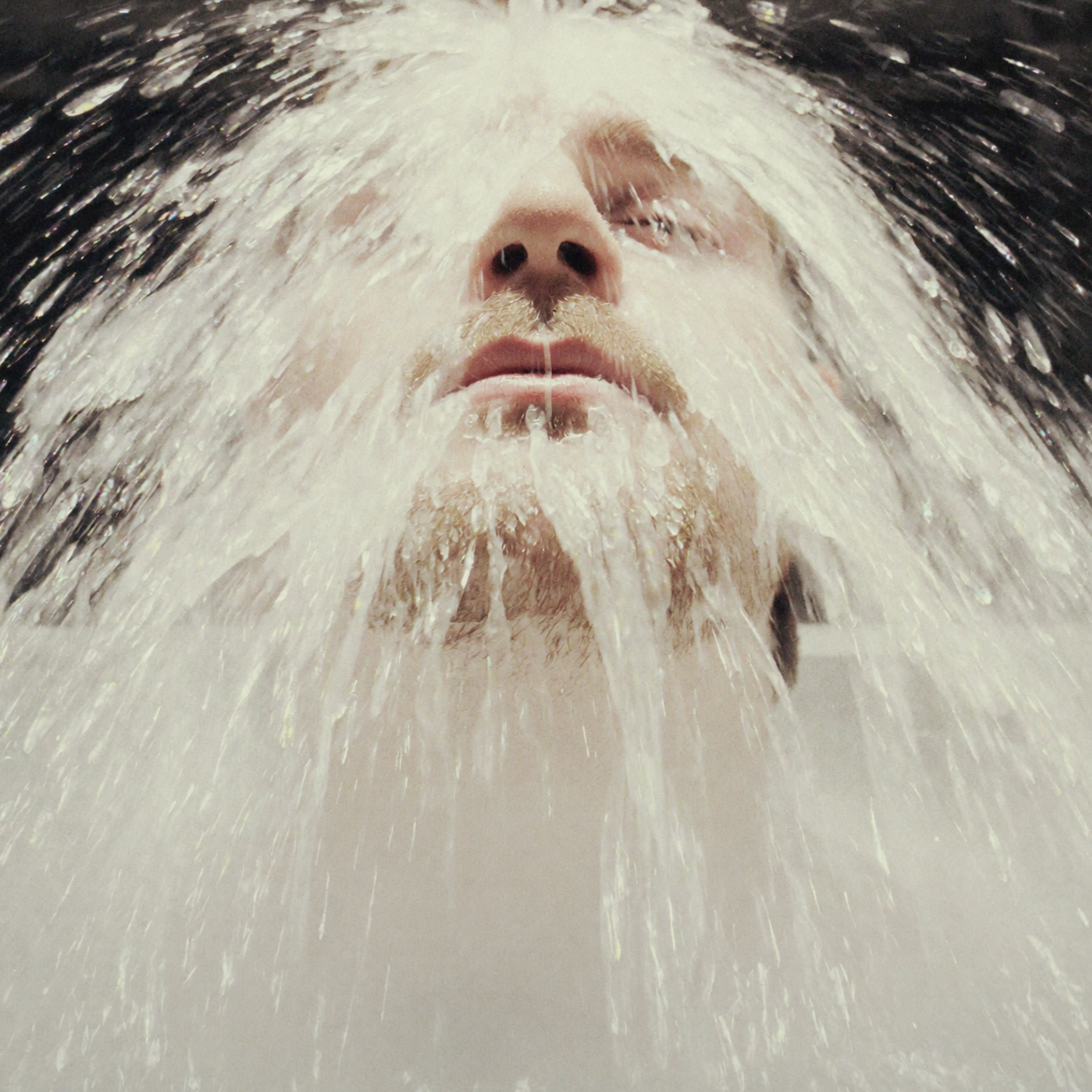 Close-up of a person's face with water cascading over it, mouth slightly open.