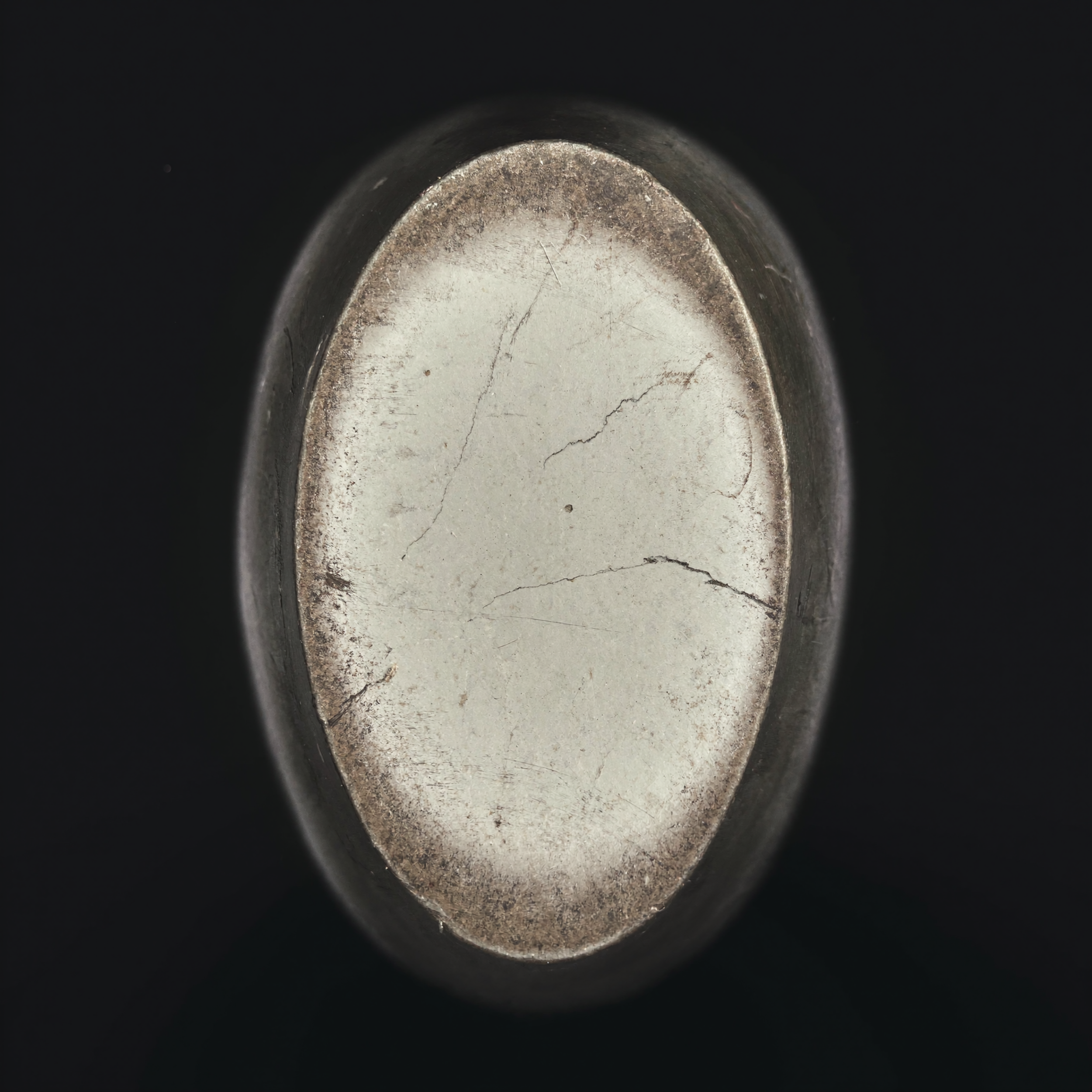 Close-up of a metallic cylindrical object with visible scratches and a worn surface, surrounded by a dark background.
