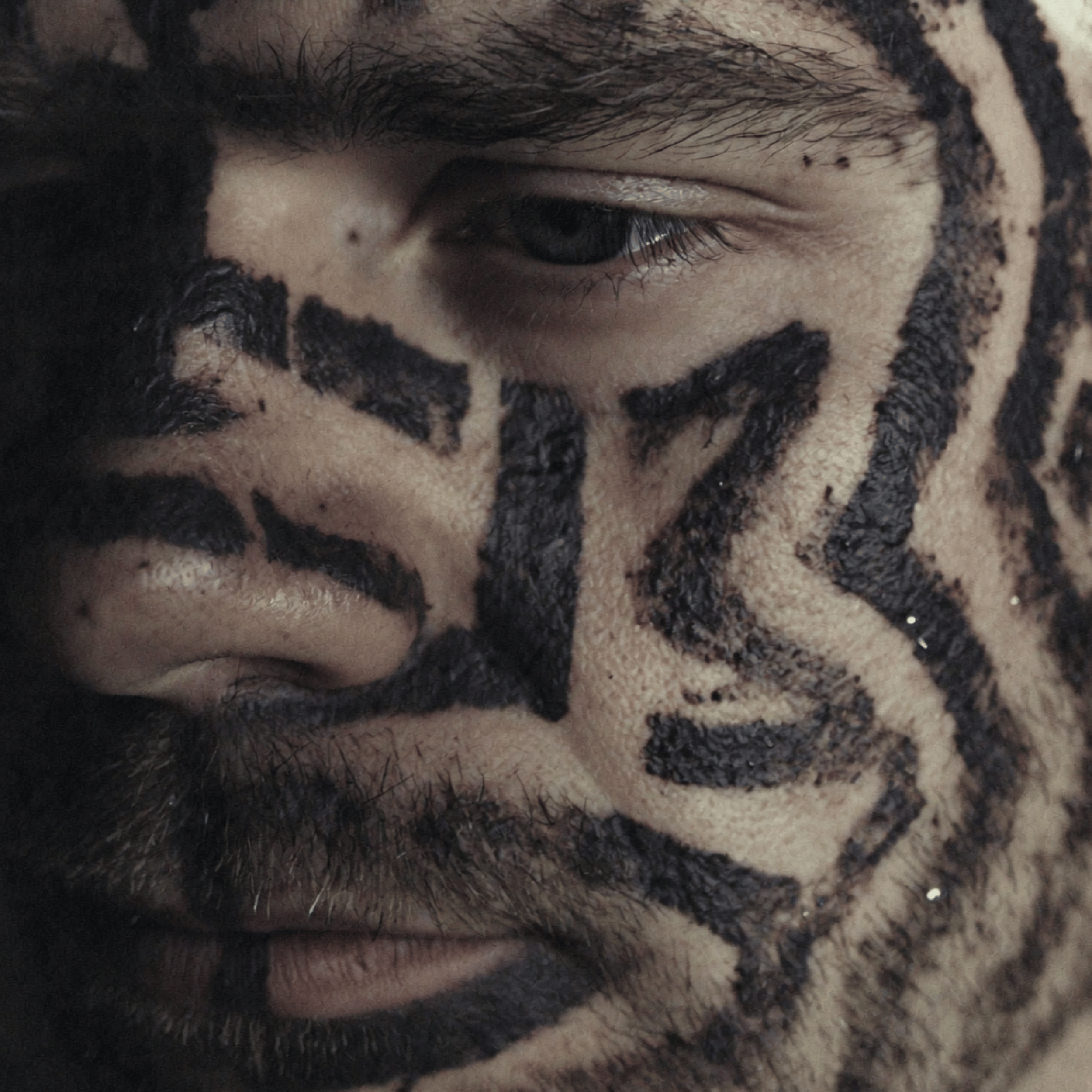 Close-up of a person's eye, eyebrow, and surrounding skin with face paint or makeup in black designs.