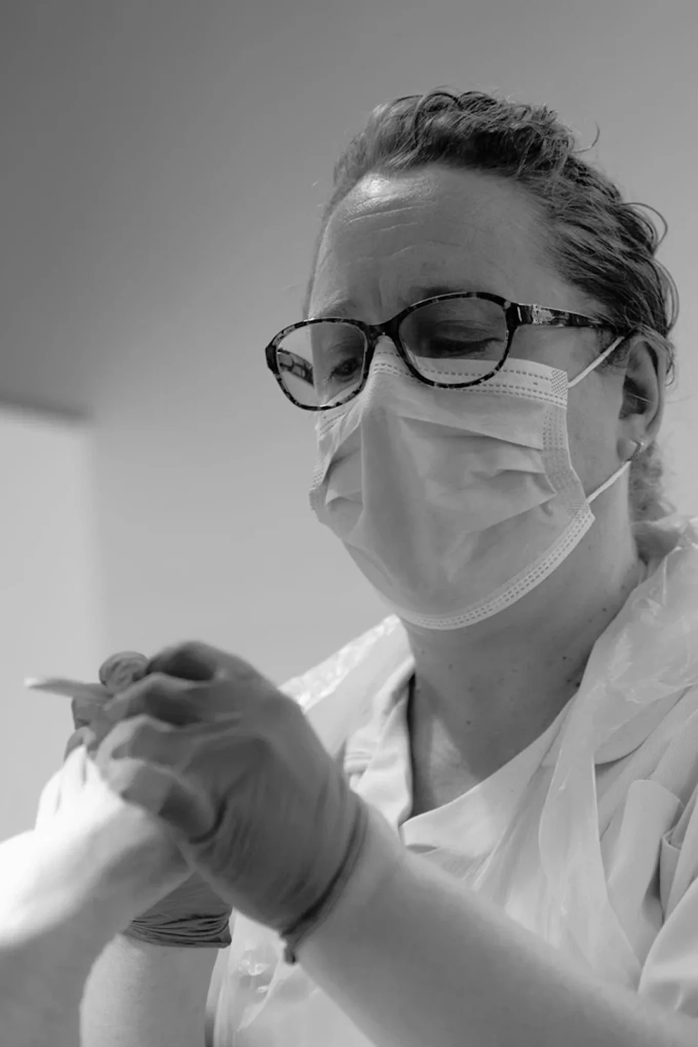Lady wearing glasses and PPE holds a foot in her hand as she files the nails